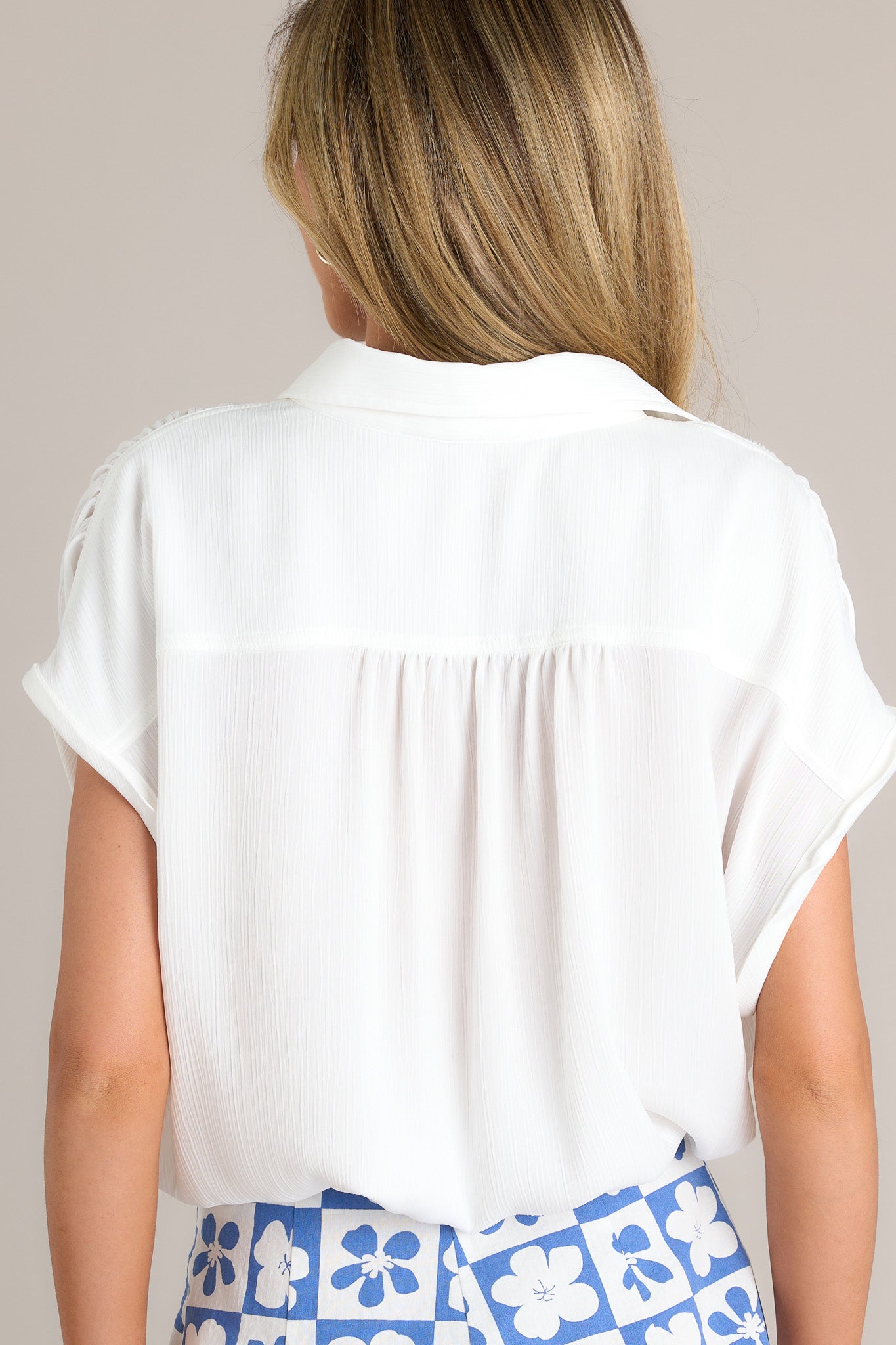 Back view of a white top highlighting the relaxed fit, cuffed short sleeves, and self-tie drawstring hemline.