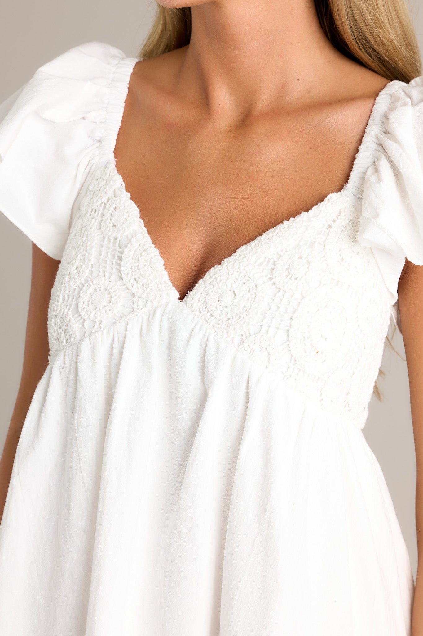 Close-up of the ivory mini dress showing the v-neckline, unique knitted pattern on the bust, and short flutter sleeves.