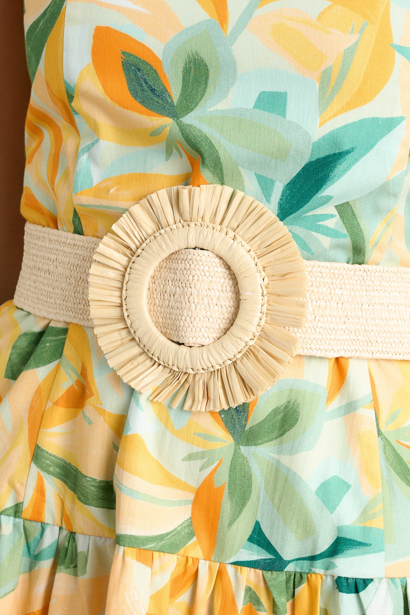 Detailed view of an ivory belt that features an stretchy band, a large round straw buckle, and a pull-through design.