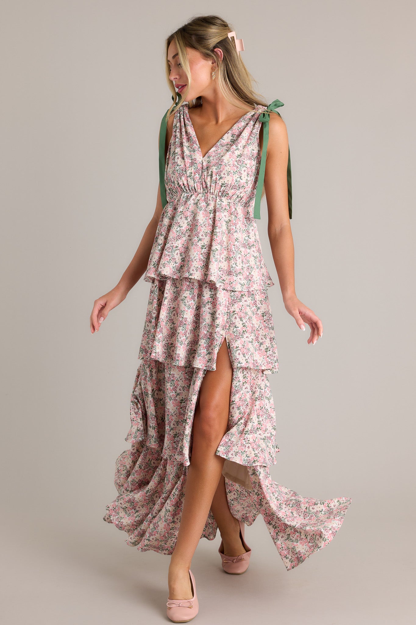 Action shot of a pink floral maxi dress displaying the fit and movement, highlighting the v-neckline, self-tie shoulder features, elastic waistline, multiple tiers, side slit, and flowing silhouette.