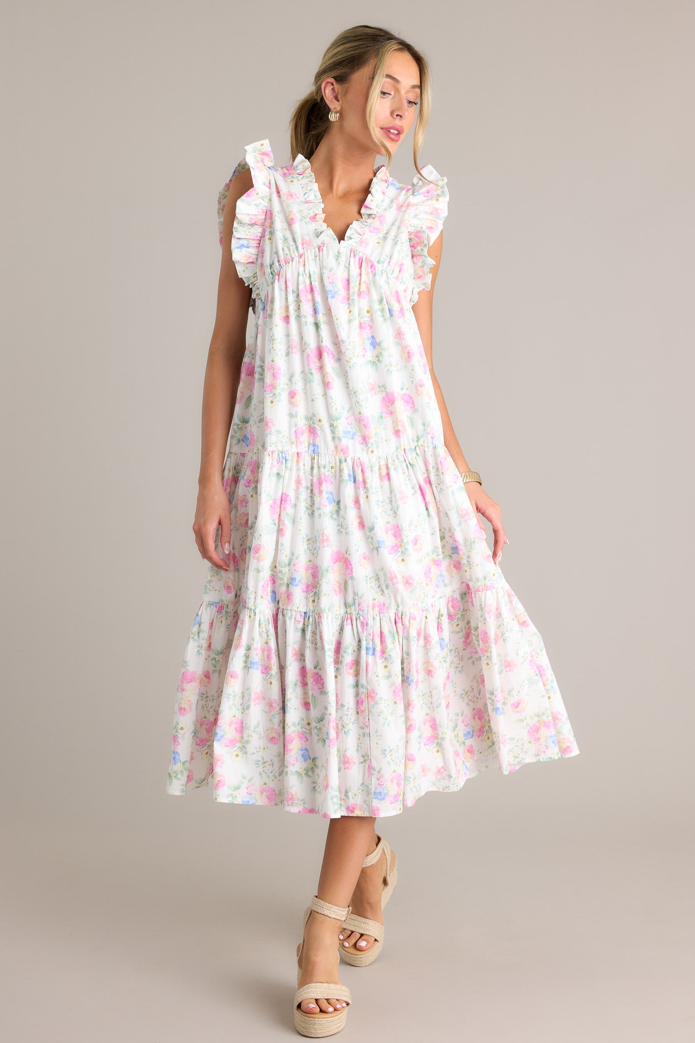 Action shot of an ivory floral midi dress displaying the fit and movement, highlighting the ruffled v-neckline, elastic waist insert, functional hip pockets, tiers, flowing silhouette, and sleeveless design.