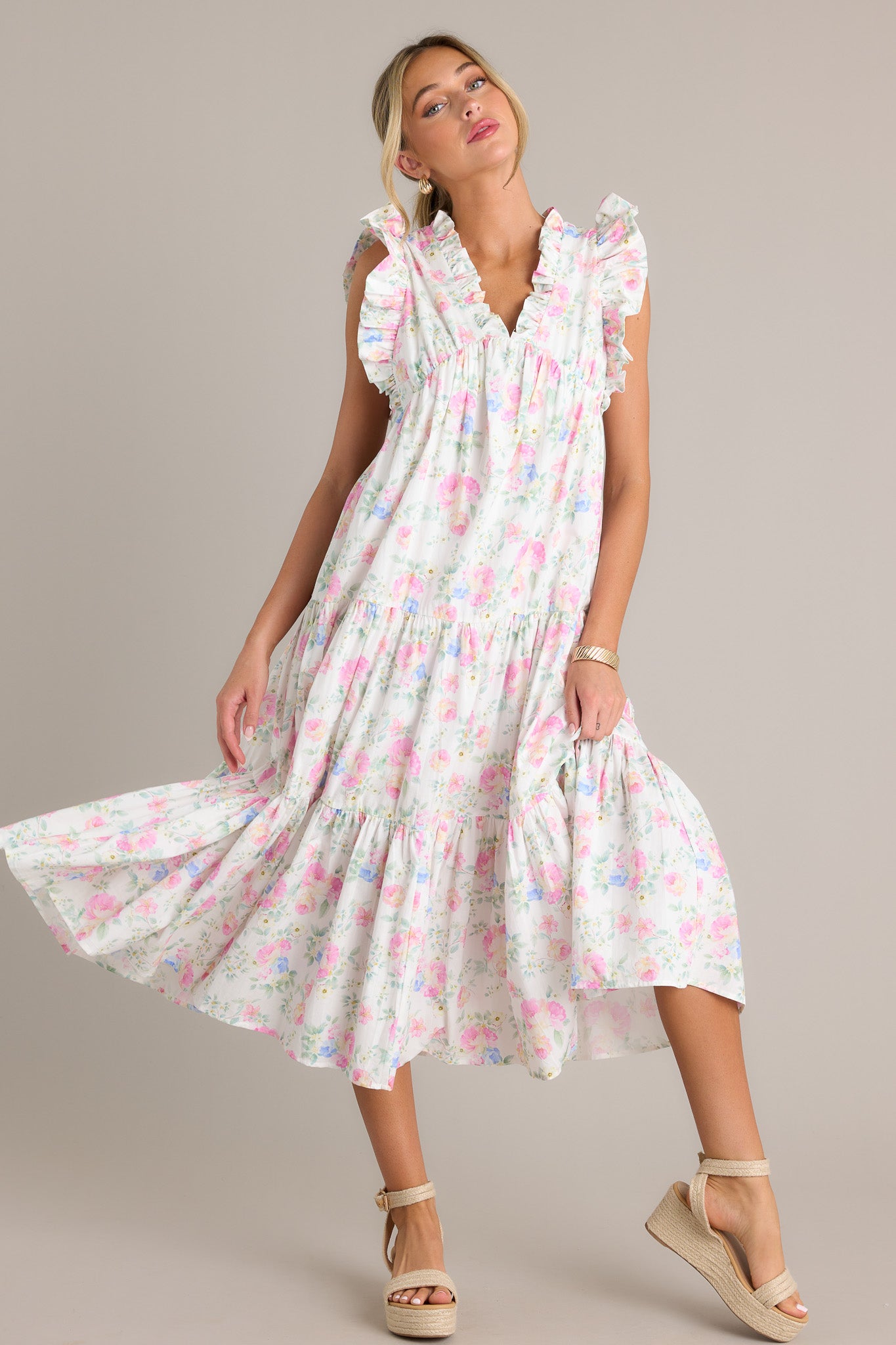 This ivory floral midi dress features a ruffled v-neckline, an elastic waist insert, functional hip pockets, tiers, a flowing silhouette, and a sleeveless design