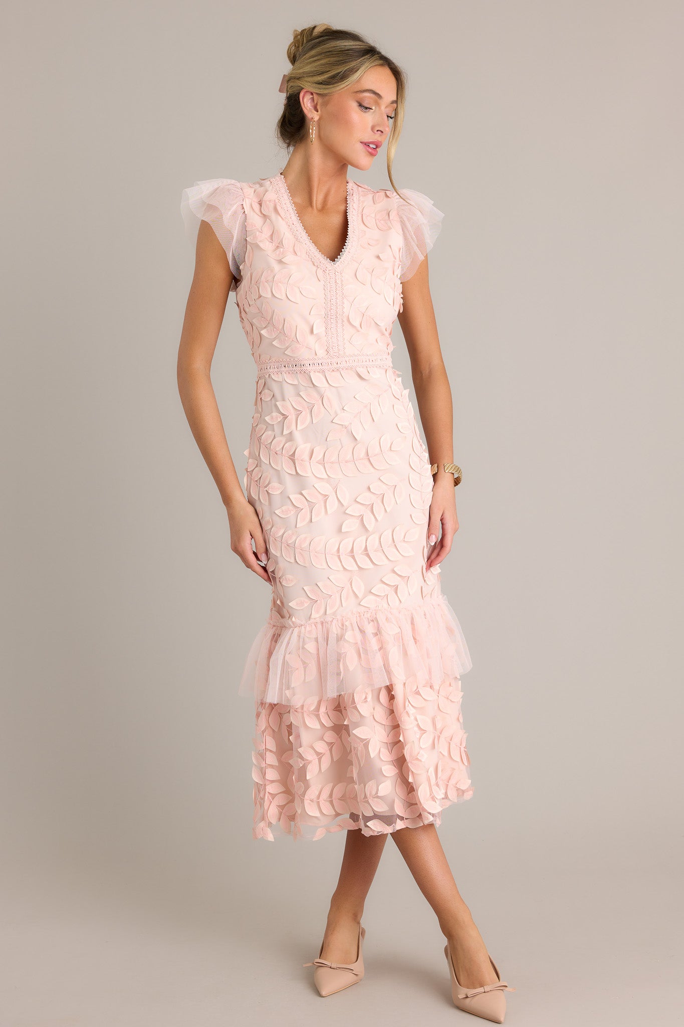 Action shot of a light pink midi dress displaying the fit and movement, highlighting the v-neckline, embroidered detailing, 3-D petals, lace tier, and lace short sleeves.