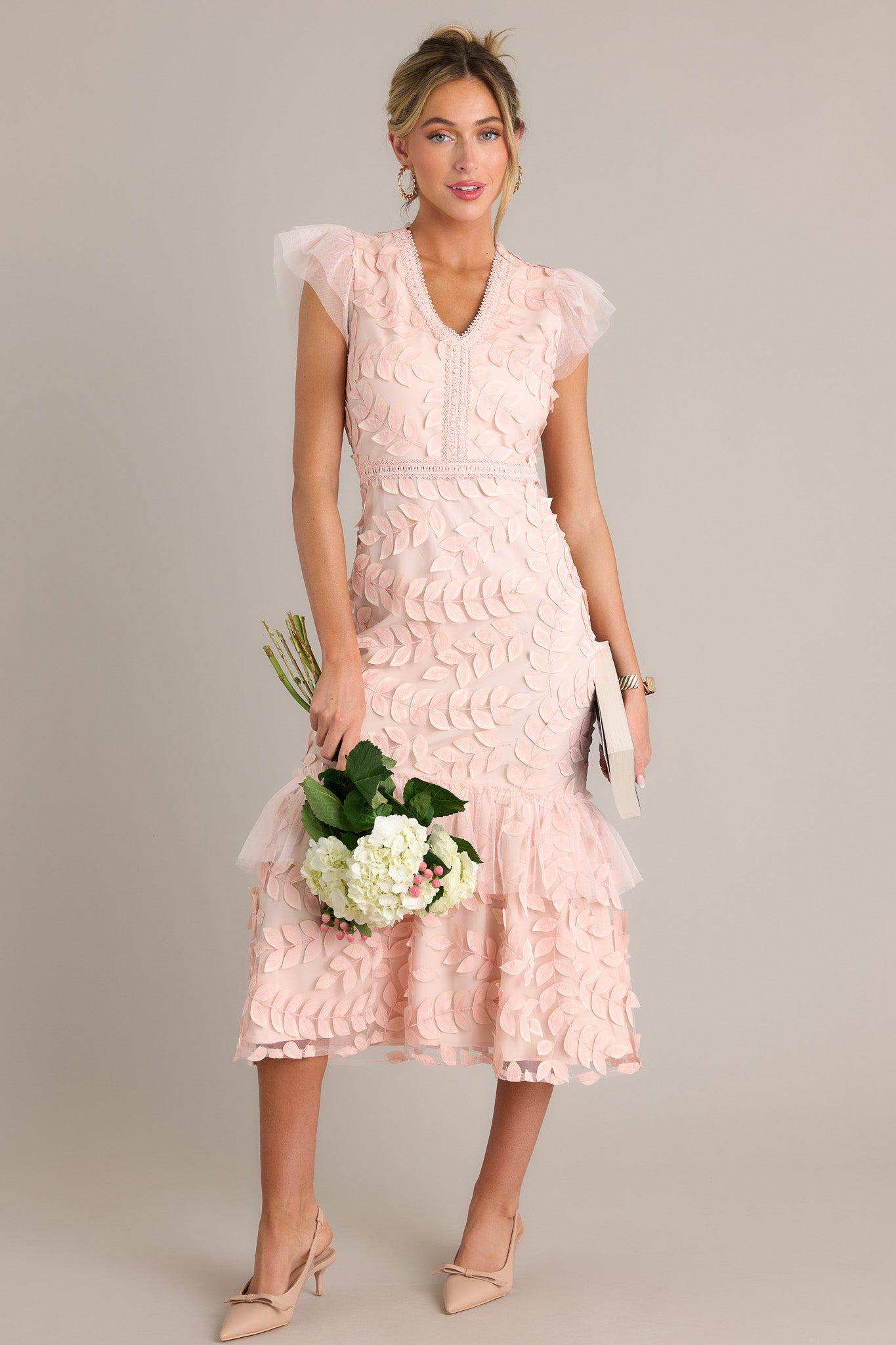  This light pink midi dress features a v-neckline, a discrete back zipper, embroidered detailing, 3-D petals throughout, a lace tier, and lace short sleeves.