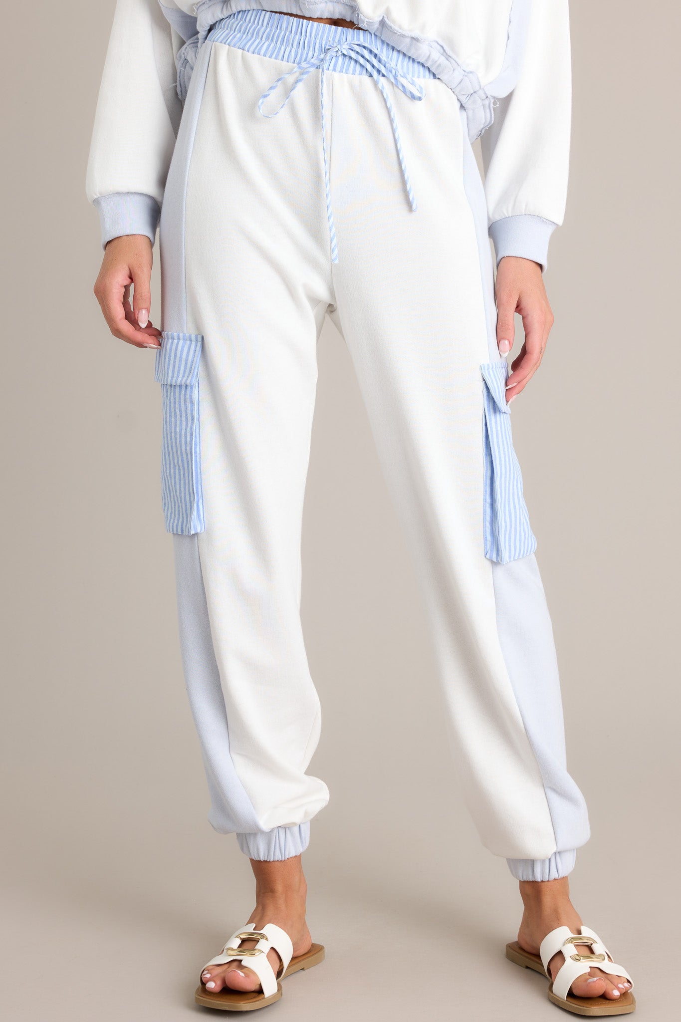 Front view of light blue joggers featuring a high waisted design, an elastic waistband, a self-tie drawstring, functional cargo pockets, and elastic cuffed ankles.