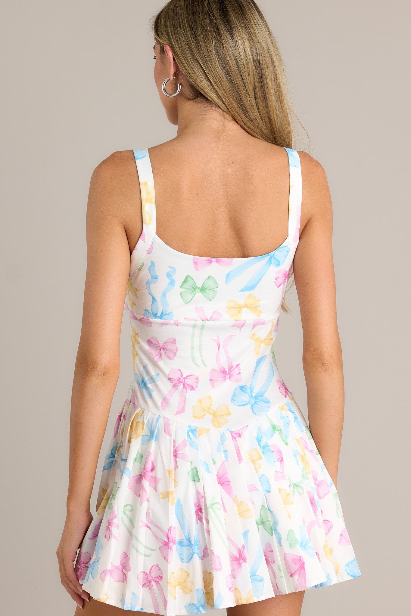 Back view of a pastel mini dress highlighting the thin straps, pastel bow pattern, and overall fit.