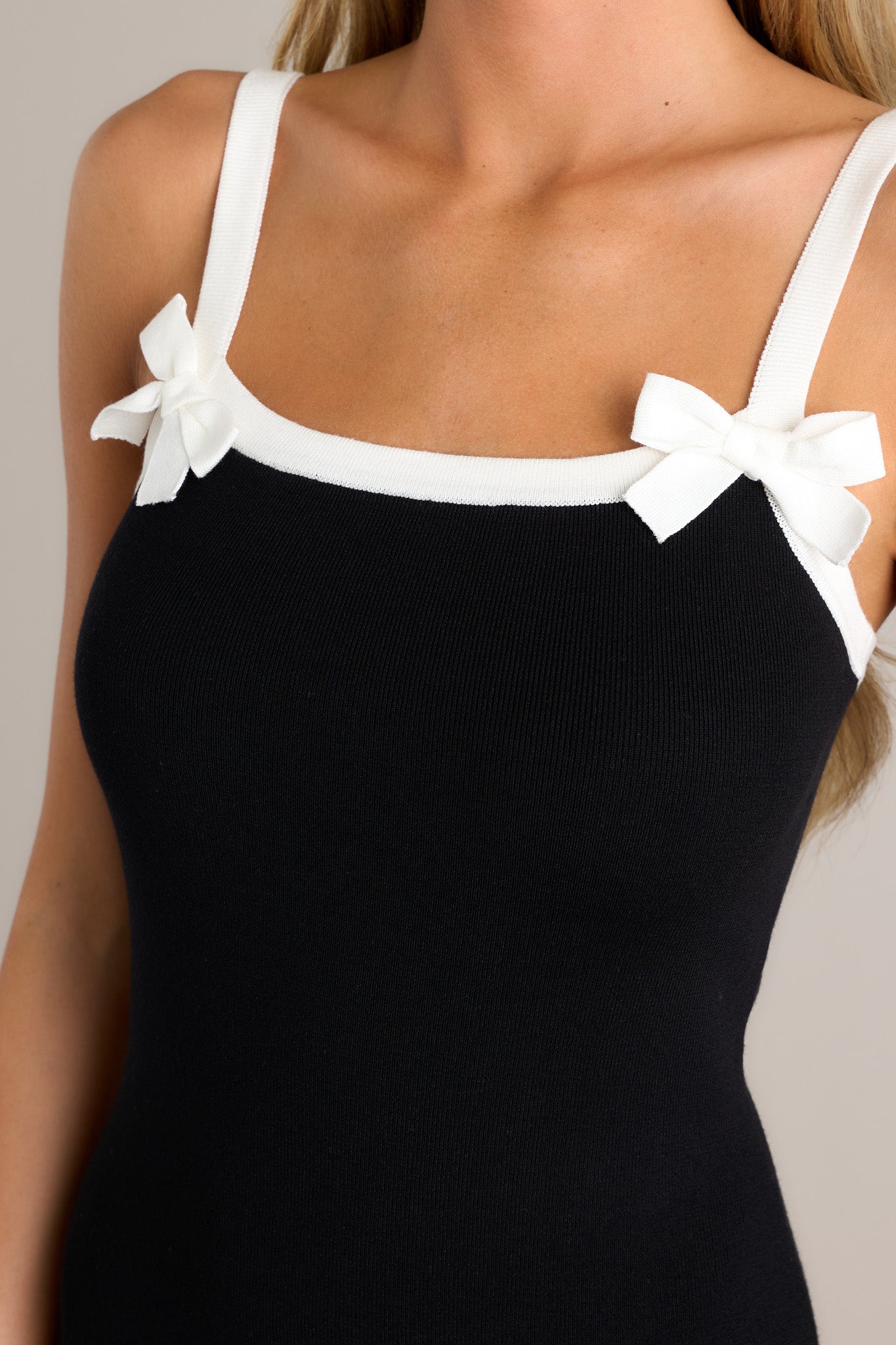 Close-up of the black mini dress showing the square neckline, bow detailing, and ribbed fabric.