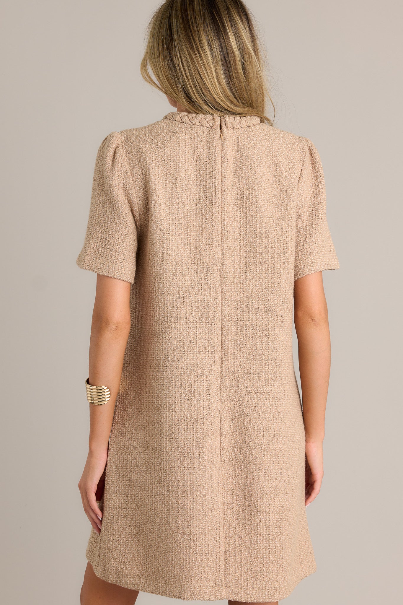 Back view of a beige mini dress highlighting the overall fit, tweed material, and discrete back zipper.