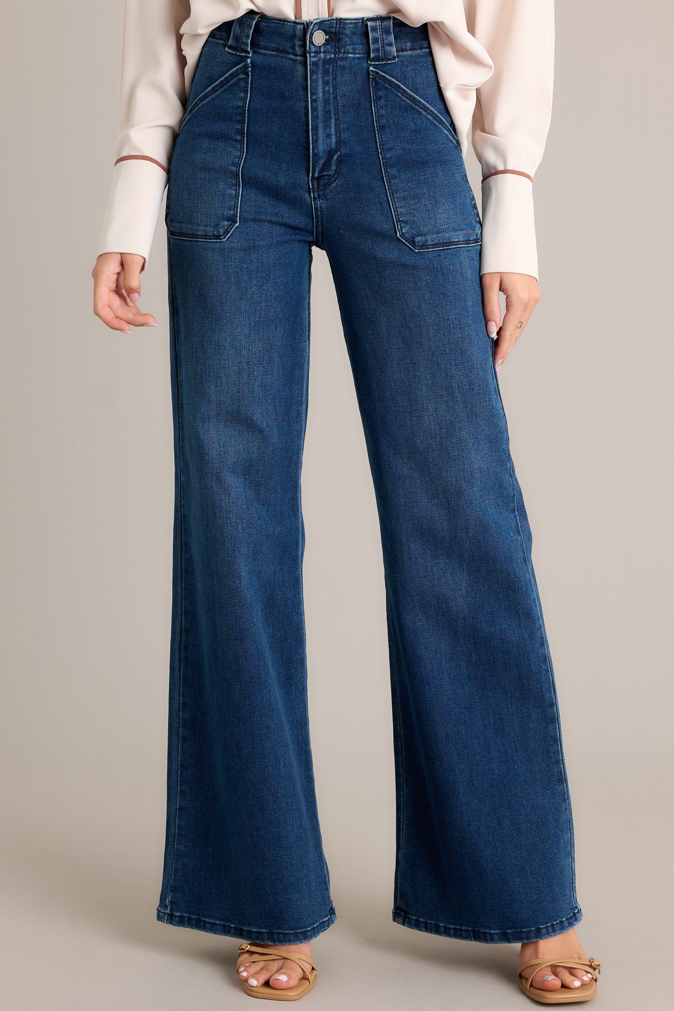 Close up view of these dark wash jeans featuring a high waisted design, classic button zipper closure, belt loops, functional front patch pockets, and a flare leg.