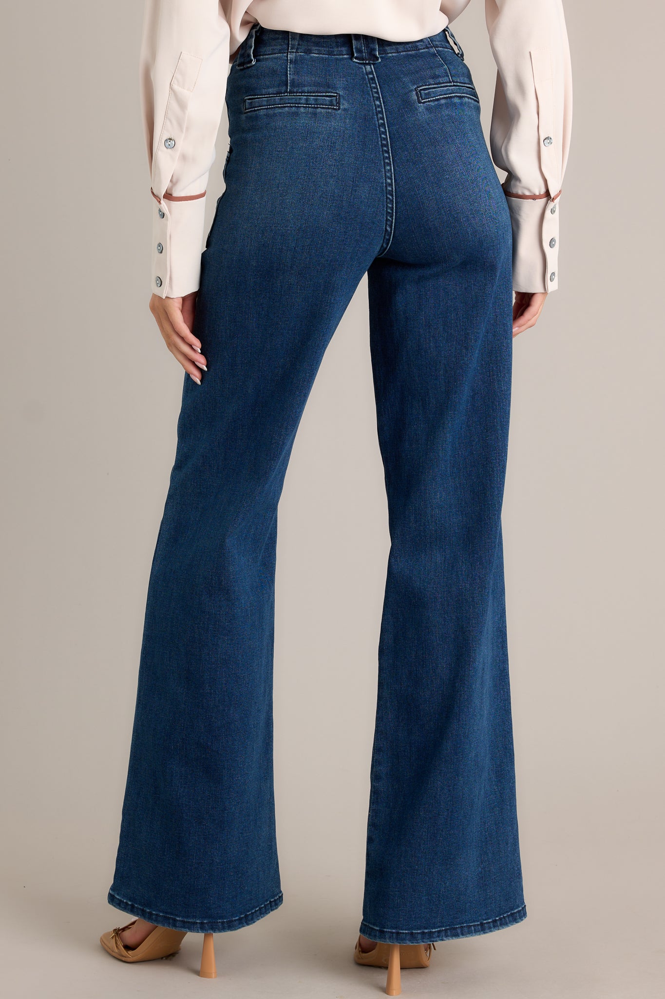 Back view of these dark wash jeans featuring a high waisted design, classic button zipper closure, belt loops, functional front patch pockets, and a flare leg.