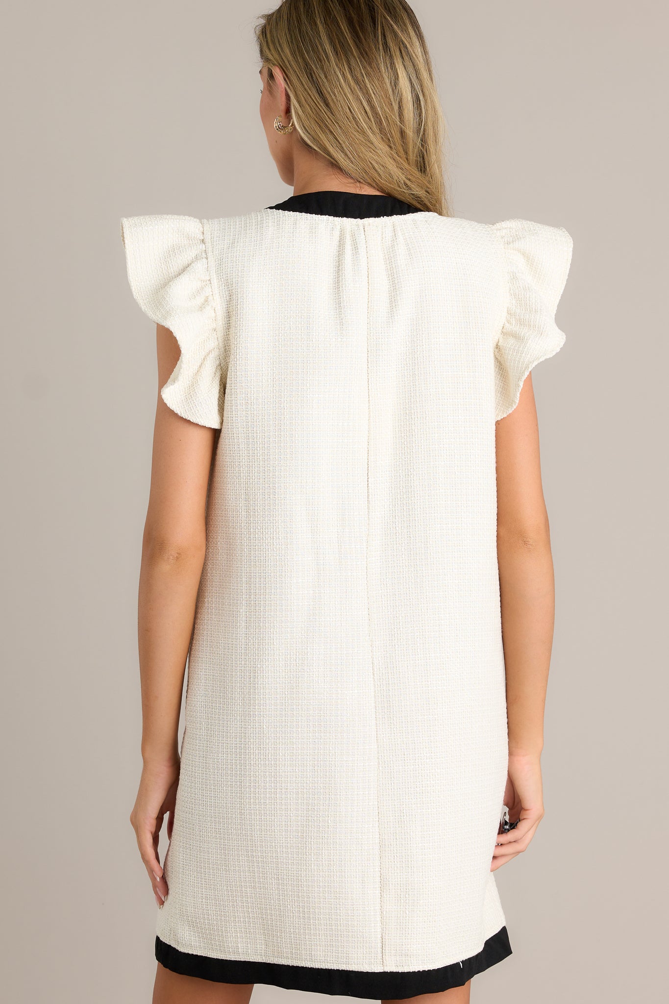 Back view of an ivory mini dress highlighting the overall fit, tweed material, and contrasting trim.