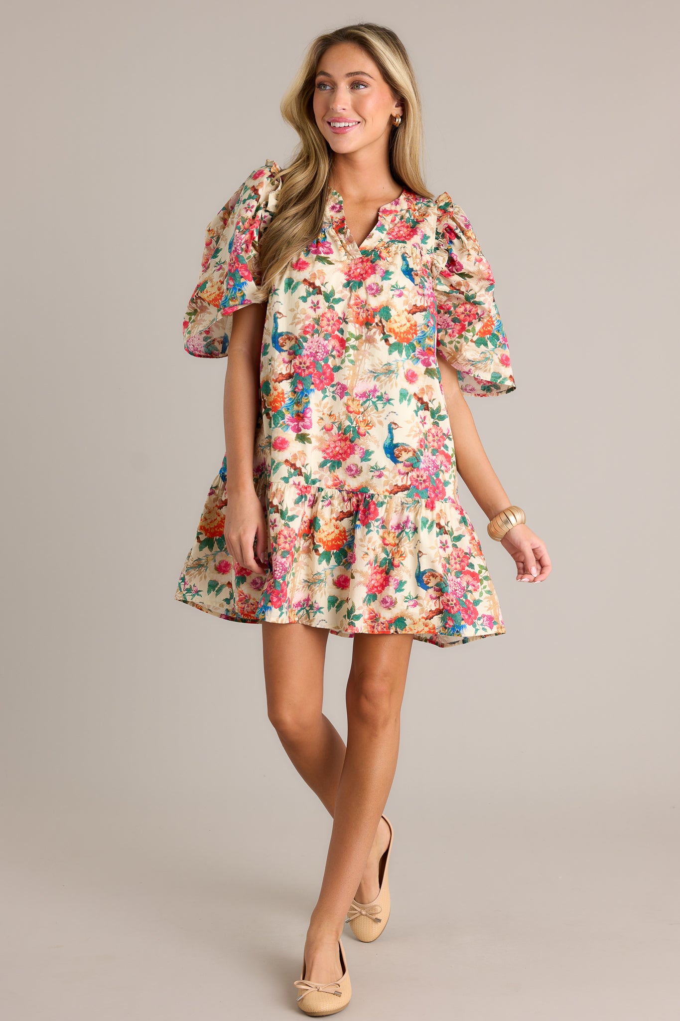 Action shot of an ivory floral dress displaying the fit and movement, highlighting the v-neckline, pleated details on the bust and hips, tiered design, functional hip pockets, and puffer sleeves.