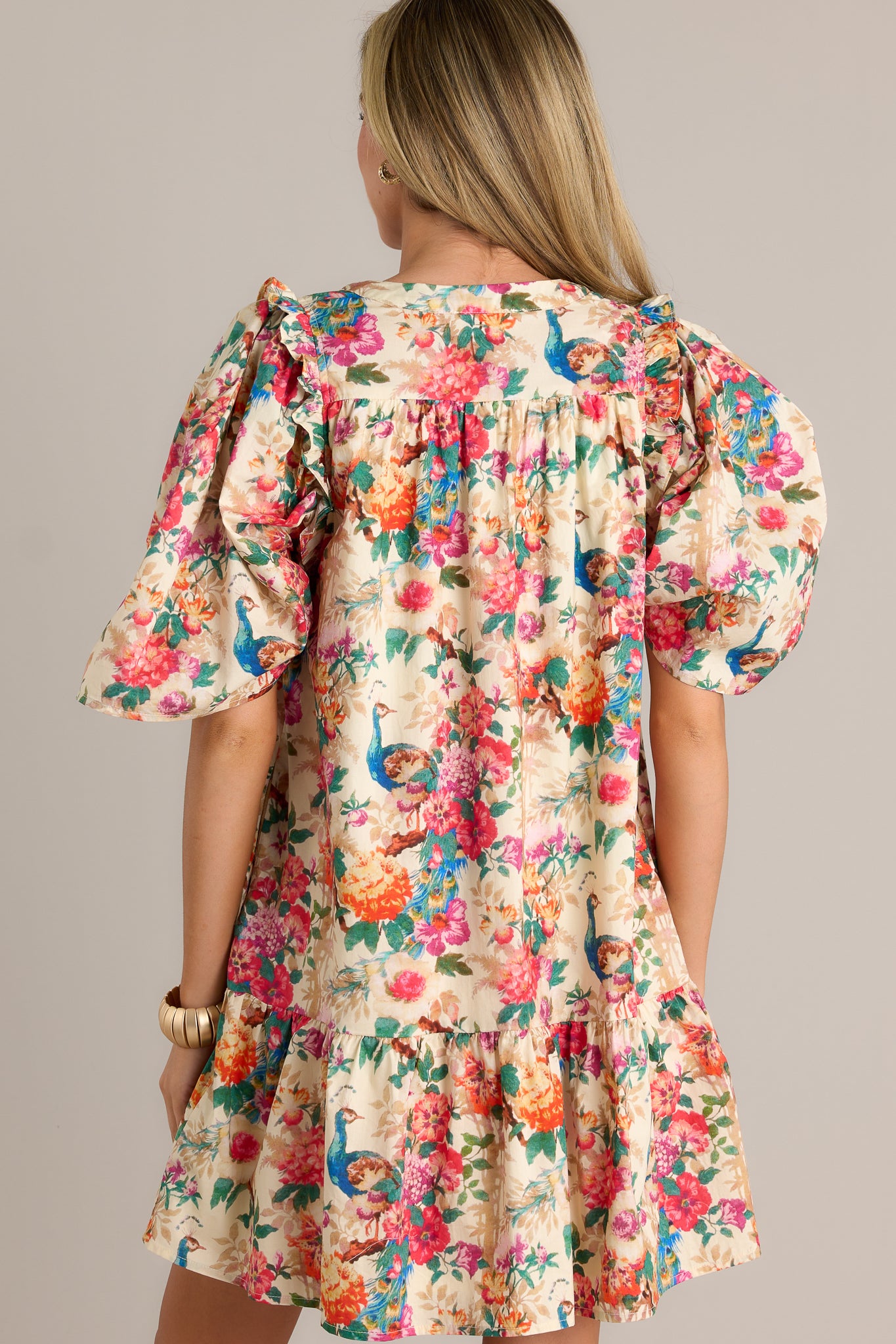 Back view of an ivory floral dress highlighting the overall fit, tiered design, and puffer sleeves.