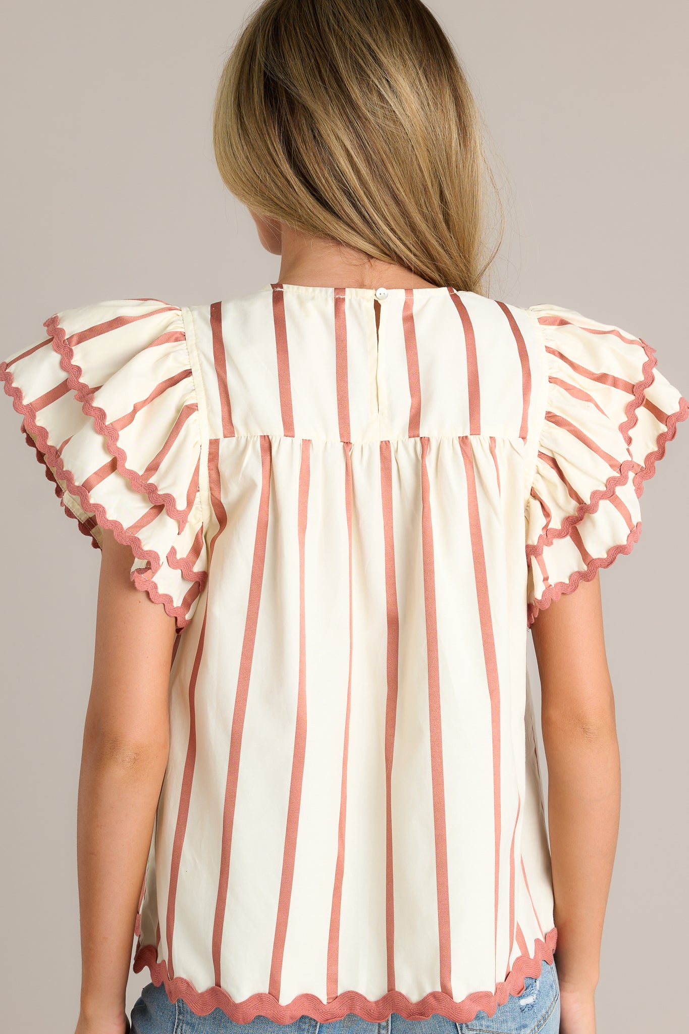 Back view of an ivory stripe blouse highlighting the overall fit, vertical stripes on the bodice, and the tiered flutter sleeves.