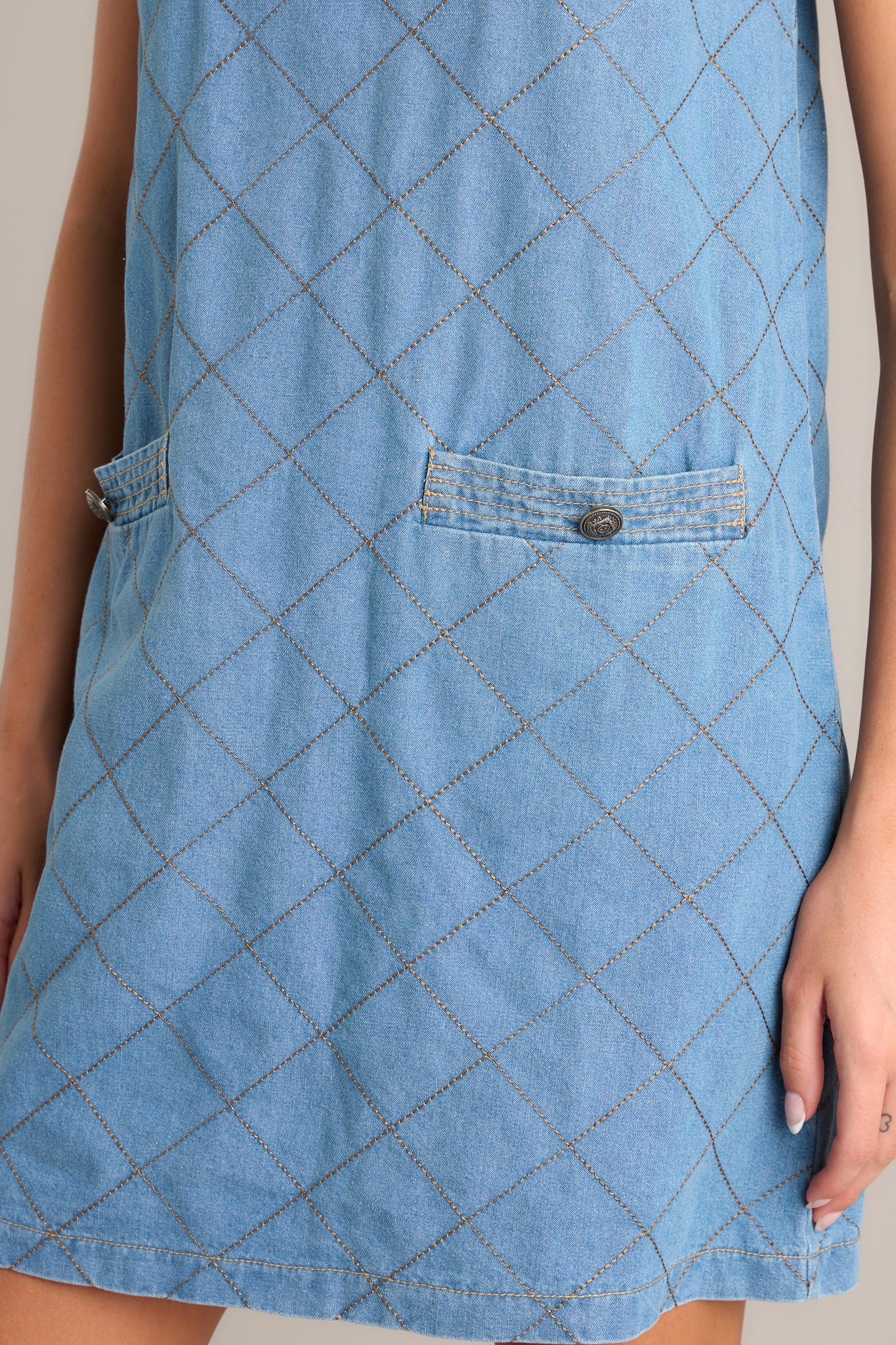 Side view of a quilted mini dress showcasing the round neckline, cognac quilted design, and functional pockets.