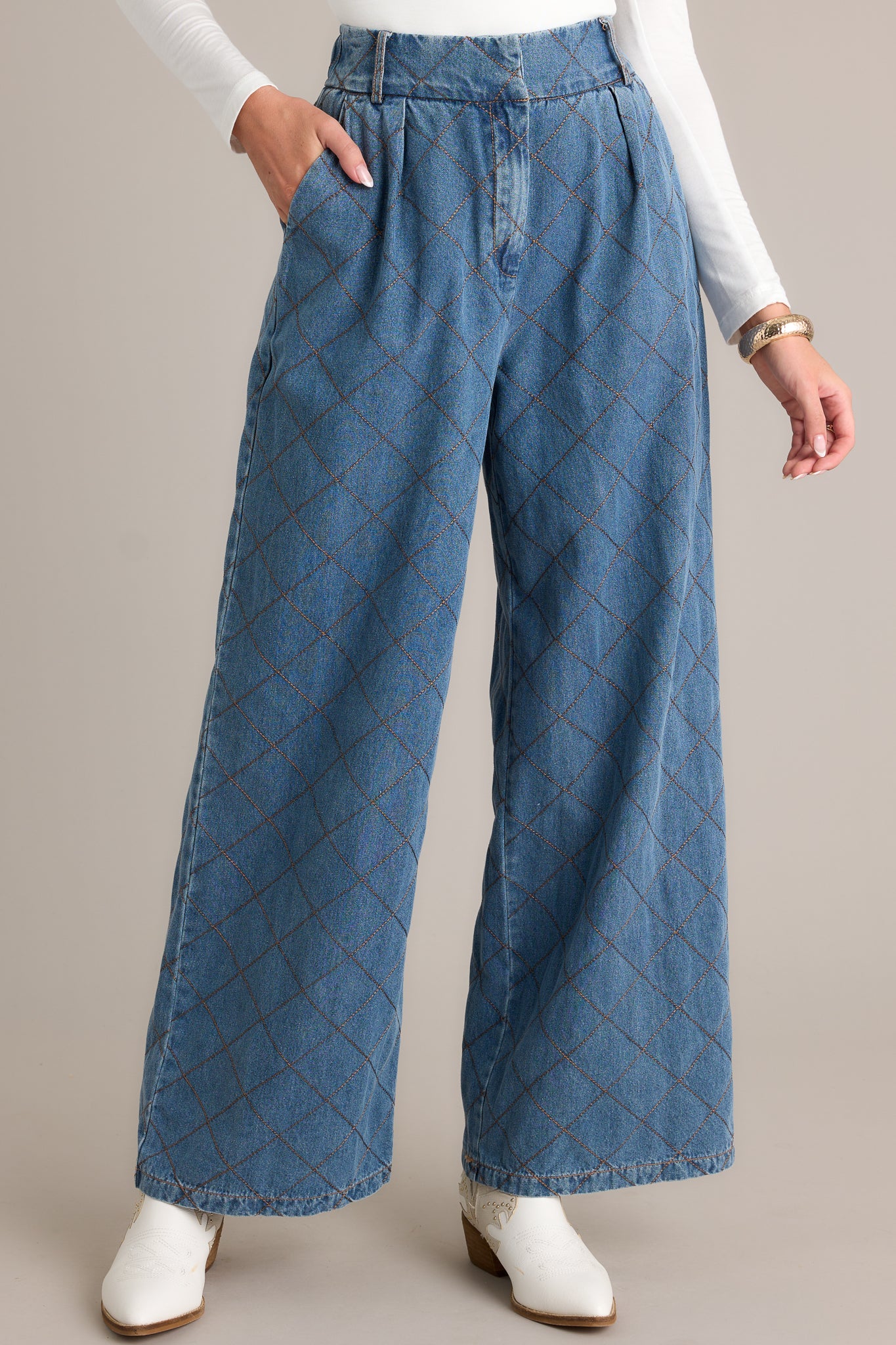 Front angled view of quilted jeans featuring a high waisted design, a hook and bar closure, functional belt loops, hip pockets, a quilted design, and a wide leg