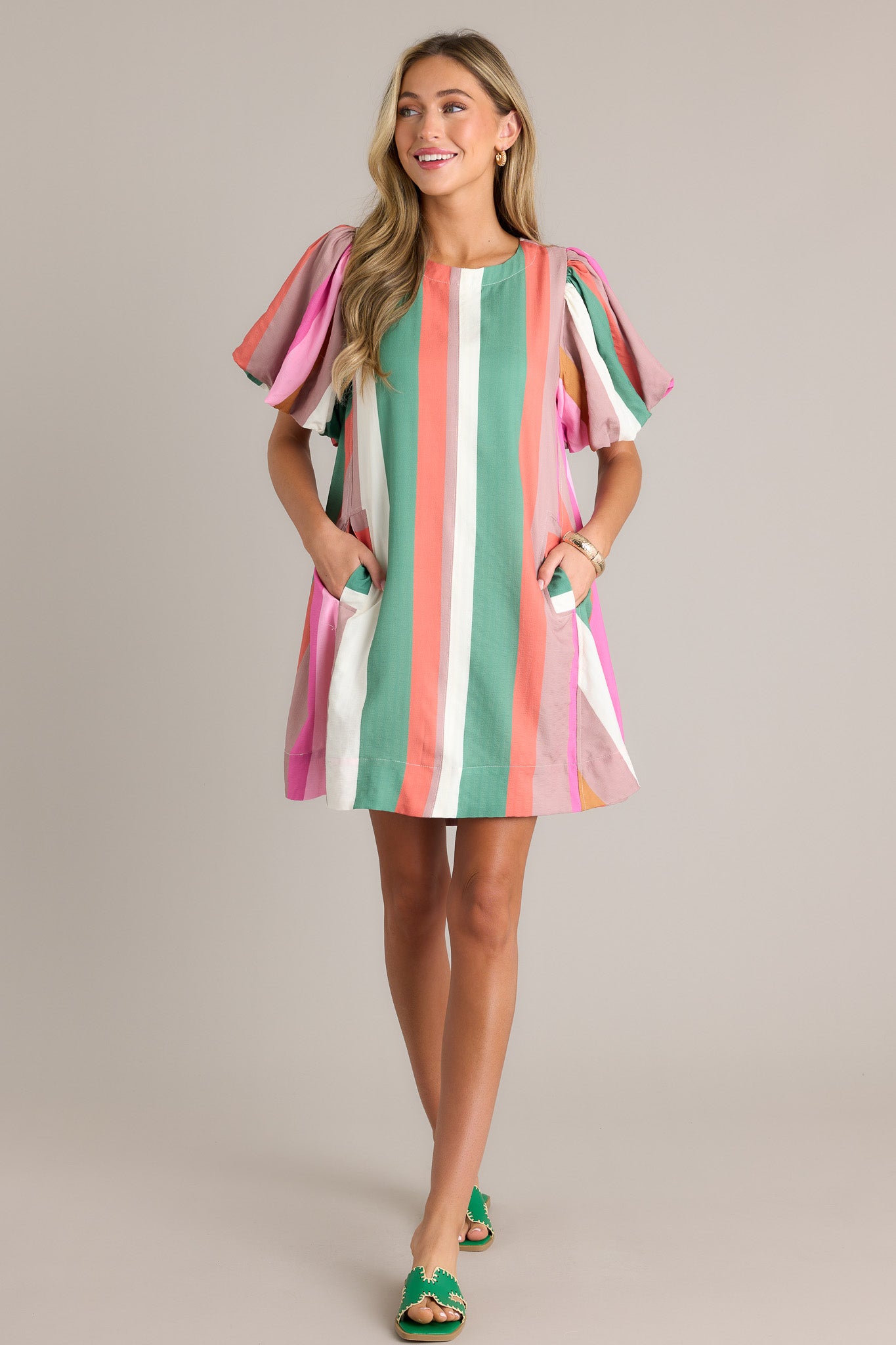 This stripe mini dress features a rounded neckline, vertical multi colored stripes, functional hip pockets, a thick hemline, and elastic cuffed puff sleeves.