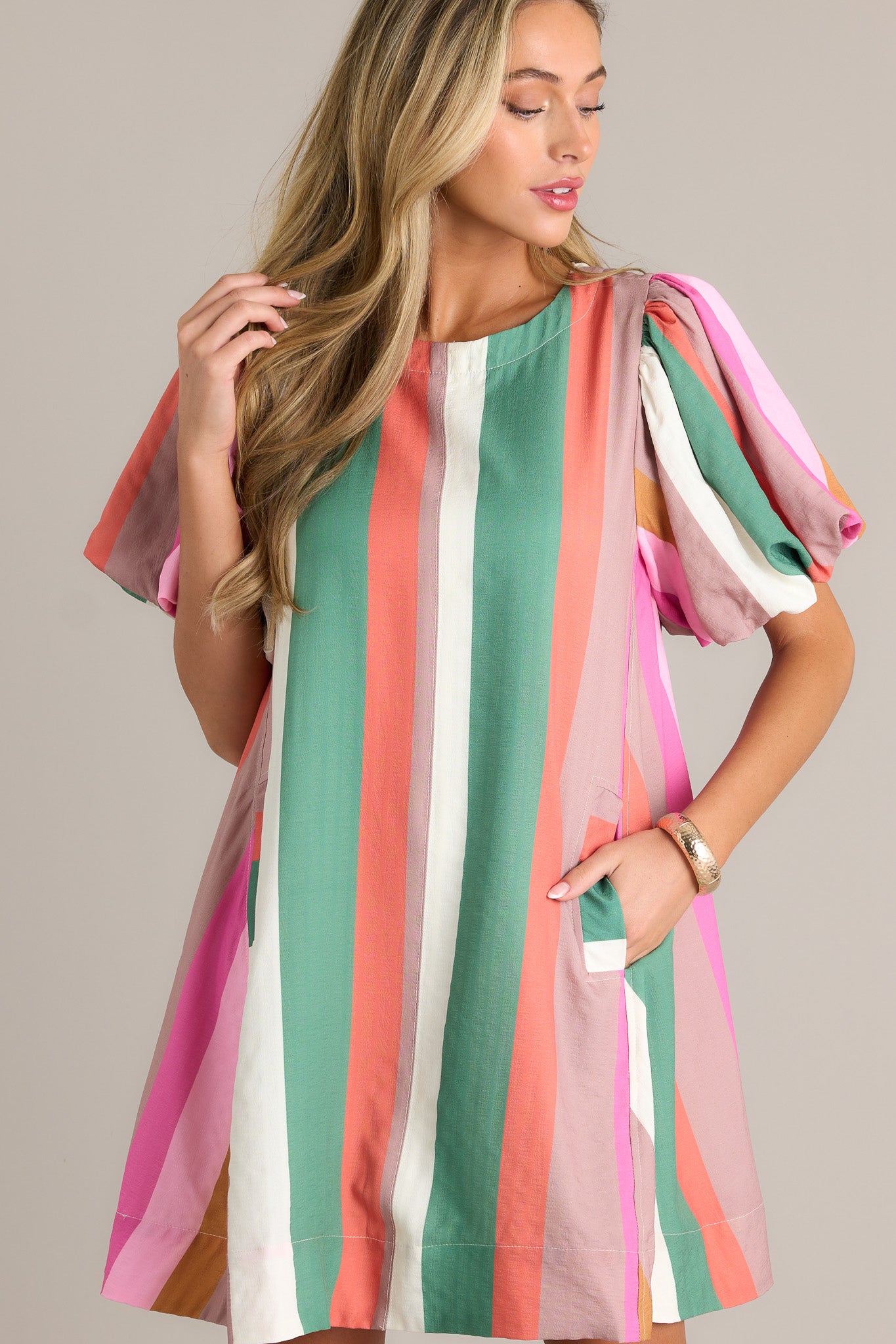 Full length view of a stripe mini dress with a rounded neckline, vertical multi-colored stripes, functional hip pockets, a thick hemline, and elastic cuffed puff sleeves