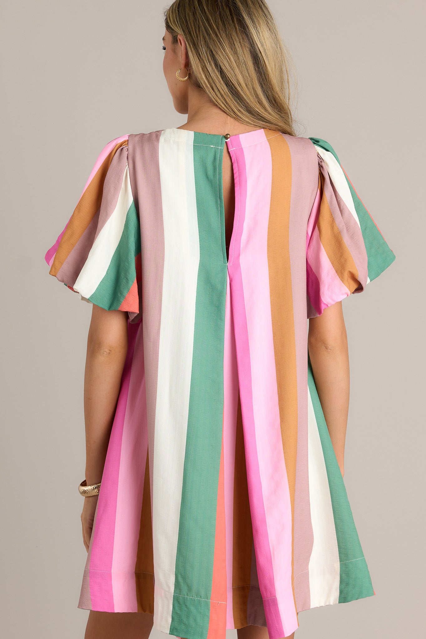 Back view of a stripe mini dress highlighting the overall fit, vertical multi-colored stripes, and elastic cuffed puff sleeves.