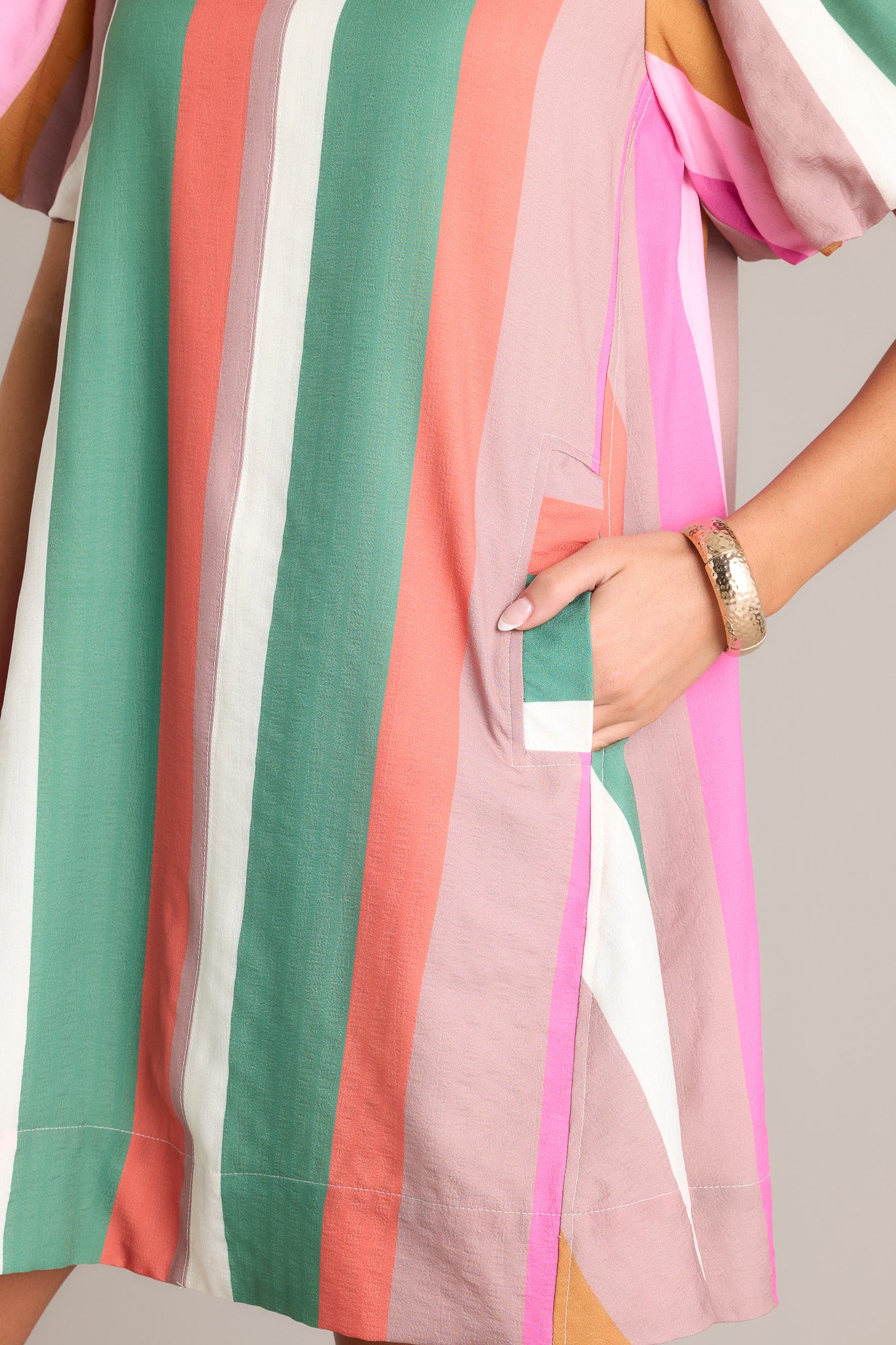 Close-up of the stripe mini dress showing the rounded neckline, vertical multi-colored stripes, and functional hip pockets.