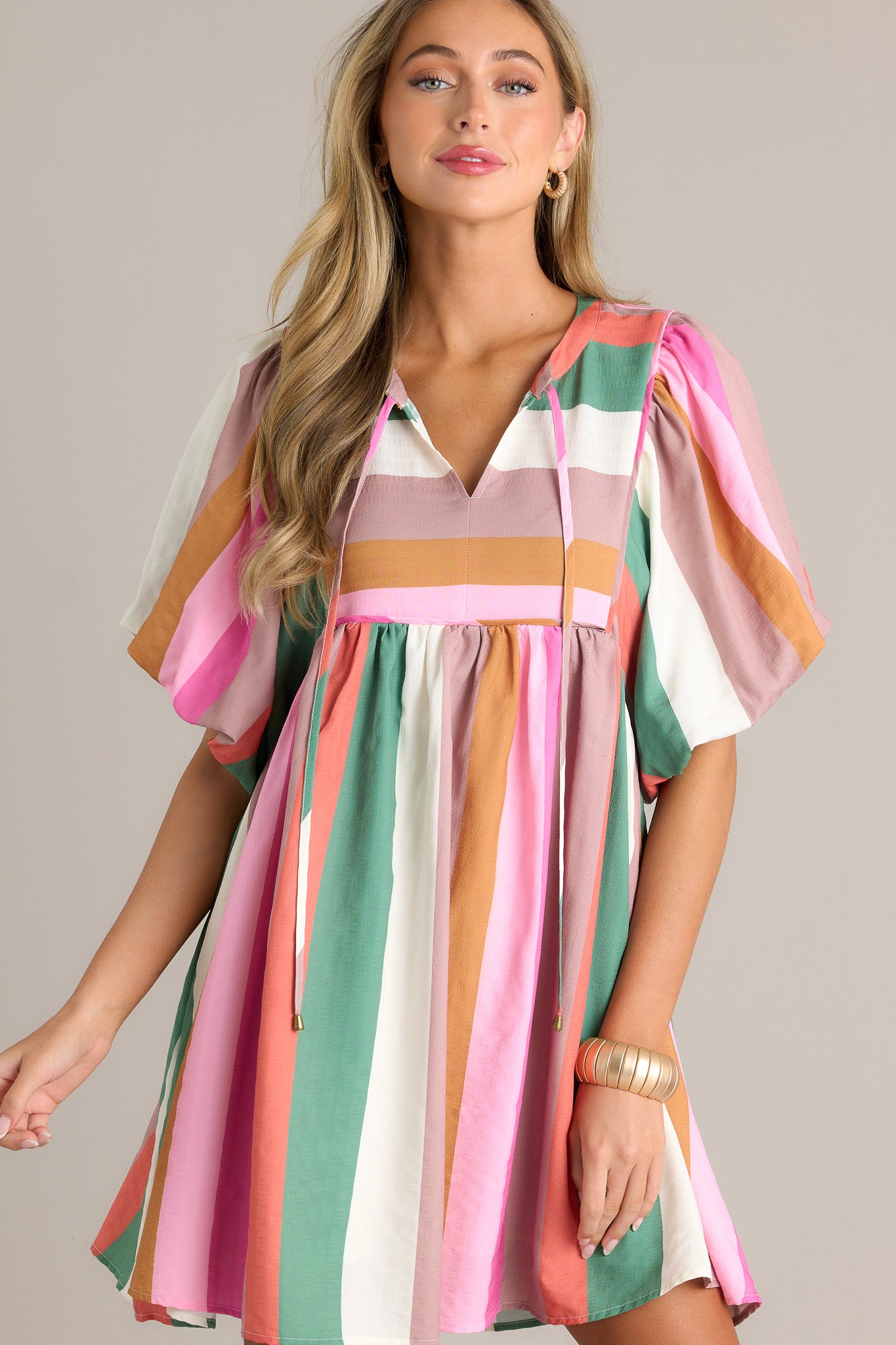 Full length view of a stripe dress with a v-neckline, a self-tie drawstring, multi-colored stripes, short elastic puffed sleeves, and a flowing silhouette