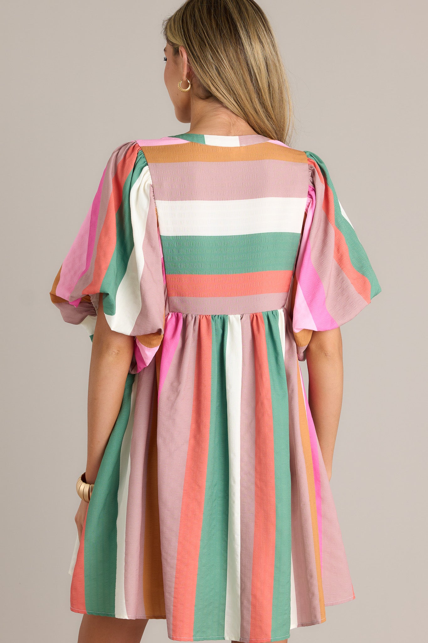 Back view of a stripe dress highlighting the overall fit, multi-colored stripes, and short elastic puffed sleeves.