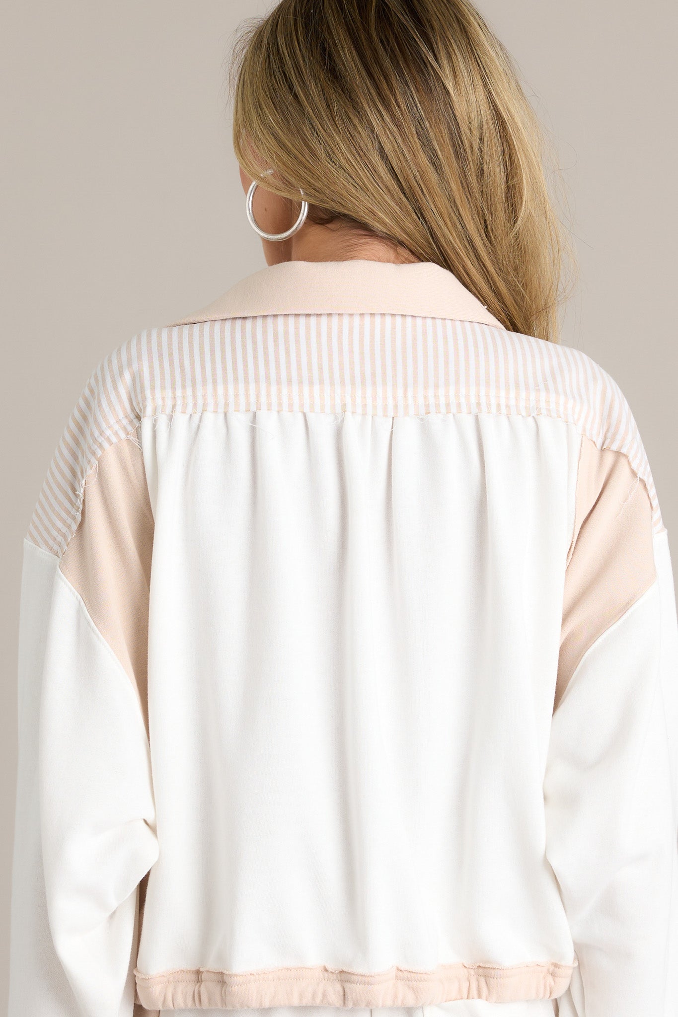 Back view of a beige cropped sweatshirt highlighting the color blocking, elastic waistband, and overall fit.