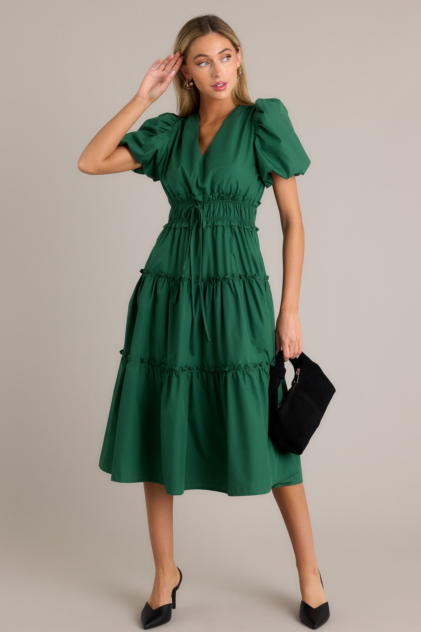 Action shot of a green midi dress displaying the fit and movement, highlighting the v-neckline, ruffled elastic waistband, self-tie waist features, functional hip pockets, tiered design, and short puffed sleeves.