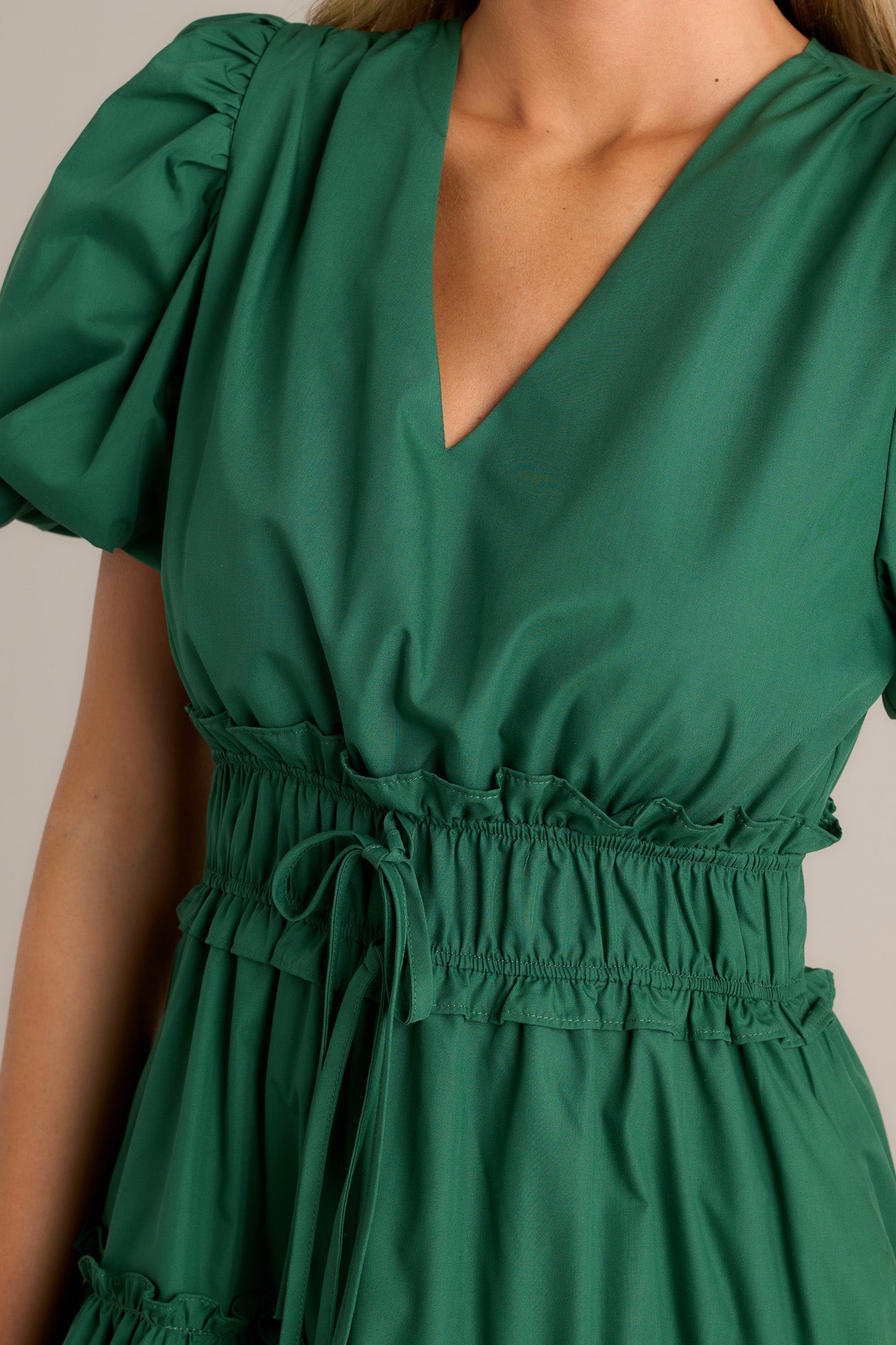 Close-up of the green midi dress showing the v-neckline, ruffled elastic waistband, self-tie waist features, and tiered design.