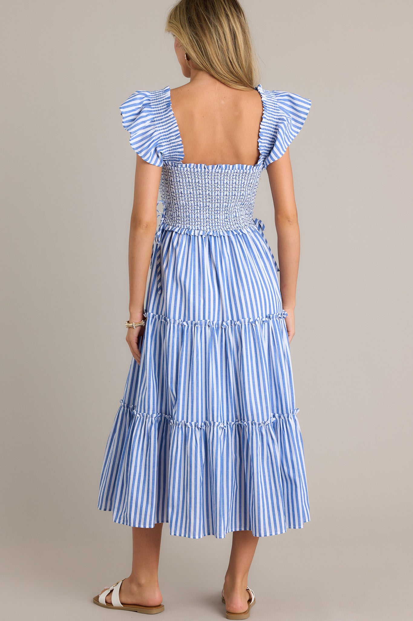 Back view of a blue stripe midi dress highlighting the overall fit, fully smocked bodice, and thick smocked straps with short flutter sleeves.