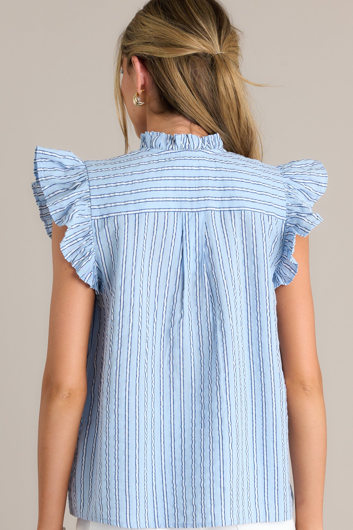 Back view of a light blue top highlighting the vertical stripes, short flutter sleeves, and overall fit.