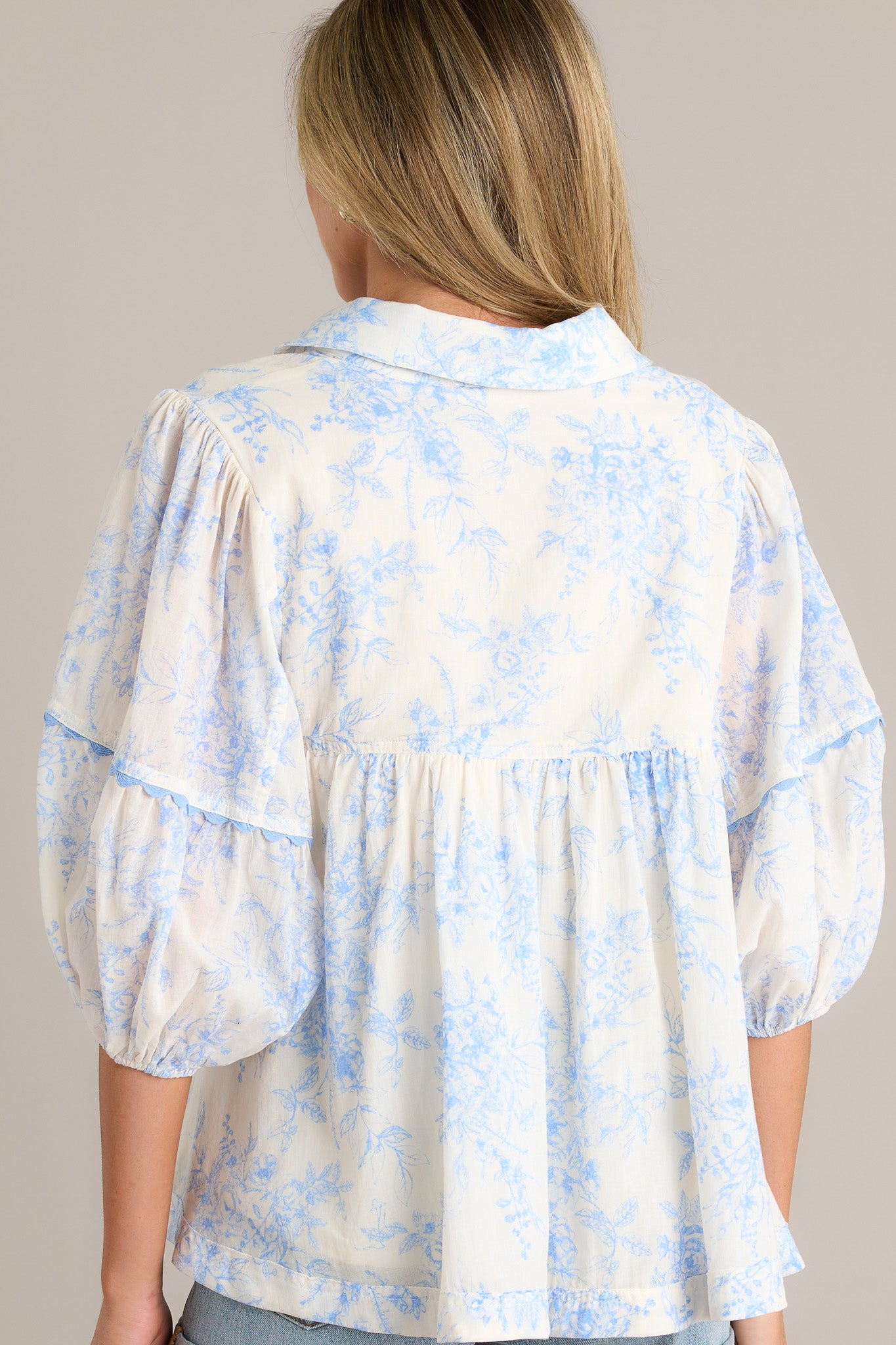 Back view of a blue toile top highlighting the overall fit, scalloped detailing, and elastic cuff 3/4 length sleeves.