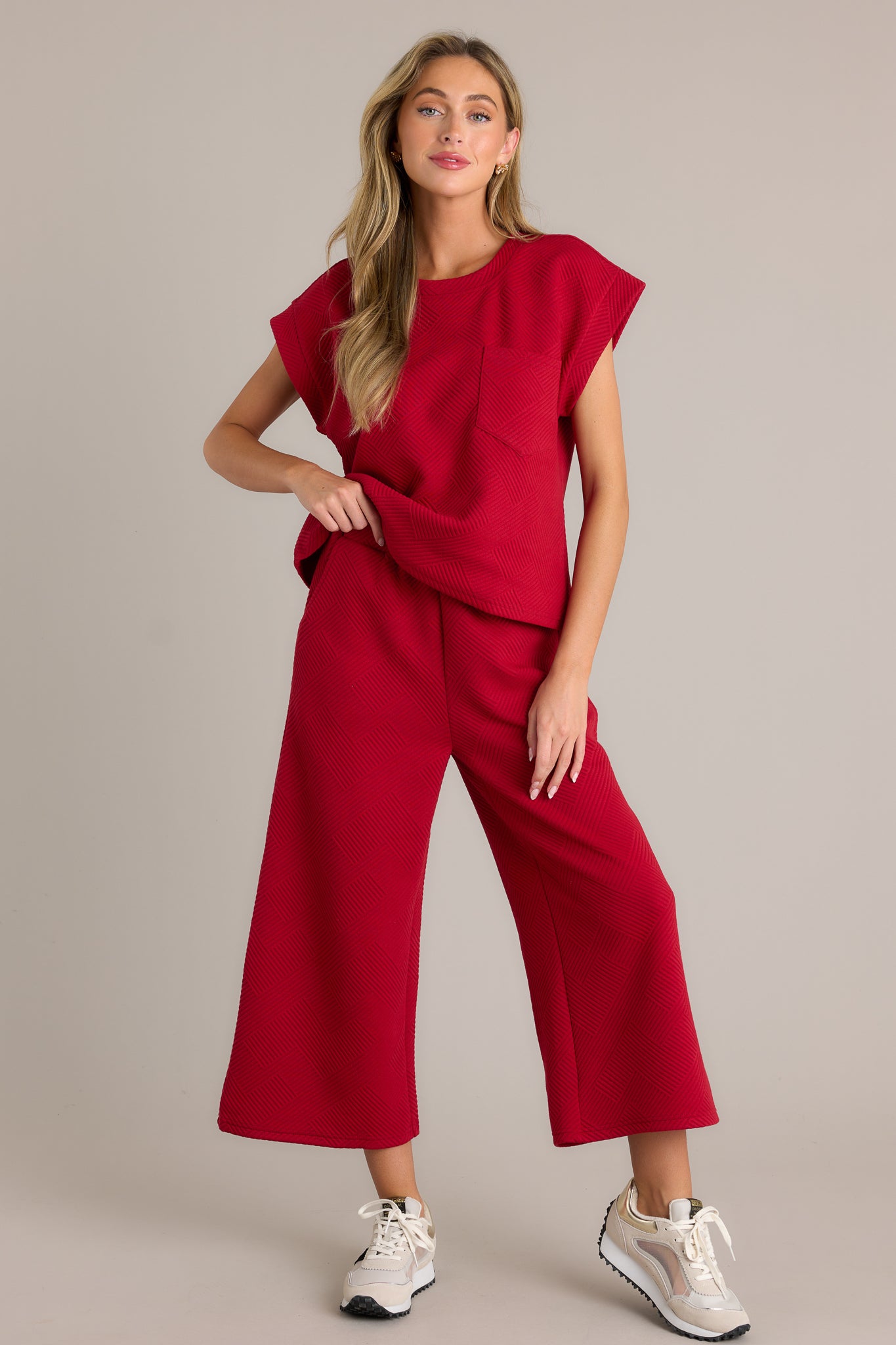 Red pants showcasing a high-waisted fit, elastic waistband, hip pockets, textured crisscross pattern, and wide-leg design.