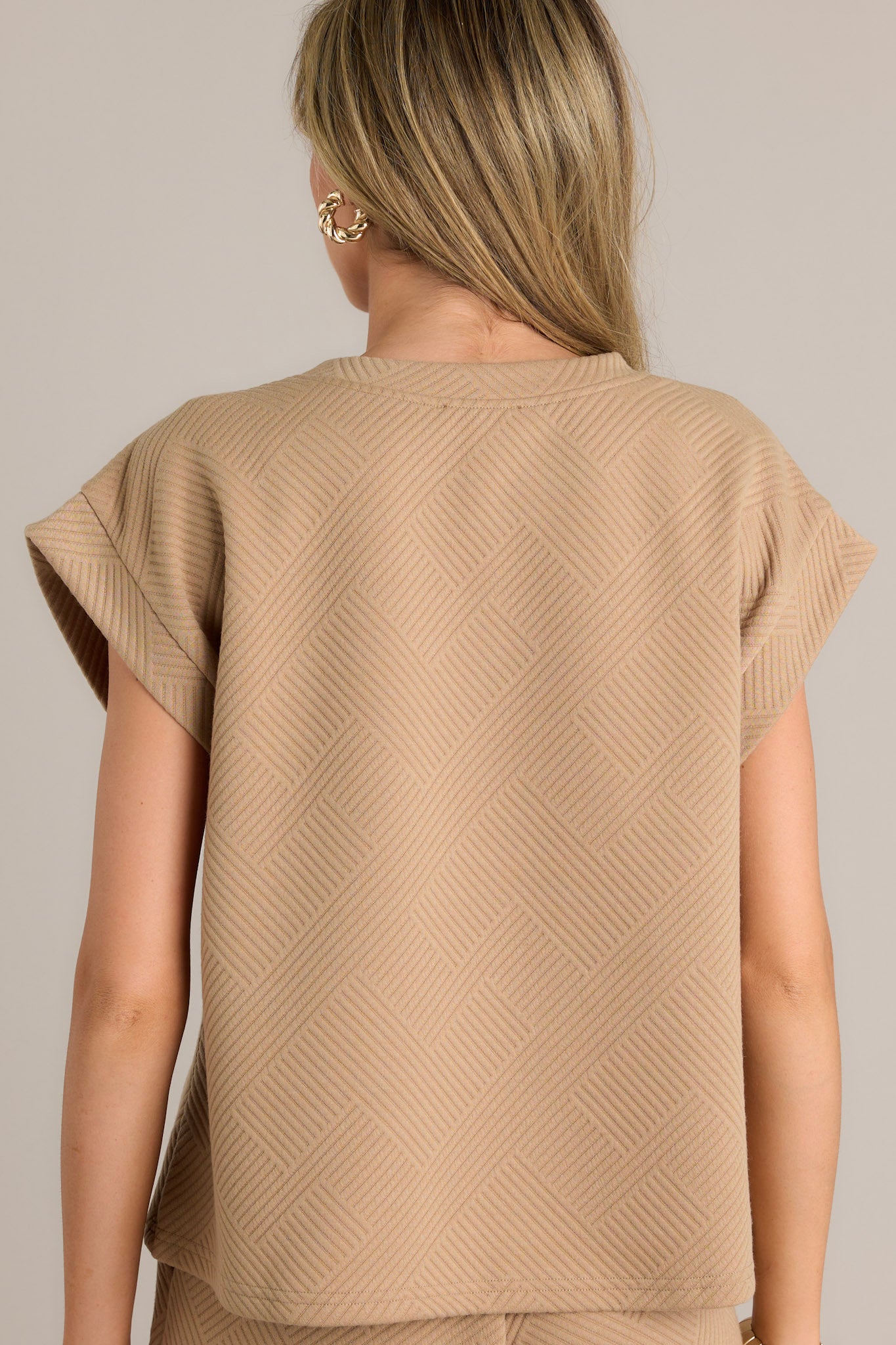 Back view of the tan top displaying the crisscross texturing and wide cuffed short sleeves.