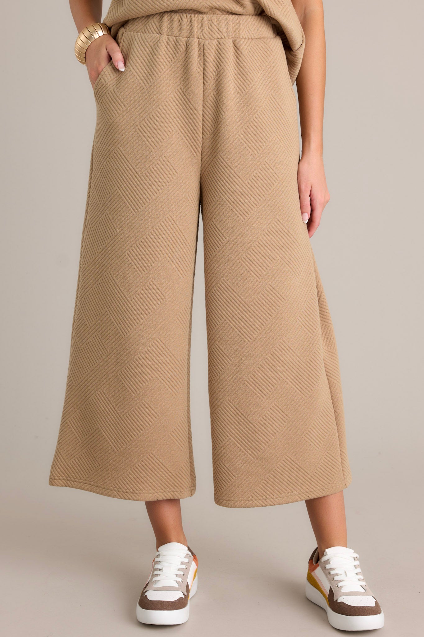 Close-up of tan pants highlighting the textured crisscross pattern, elastic waistband, and functional hip pockets with a wide-leg cut.