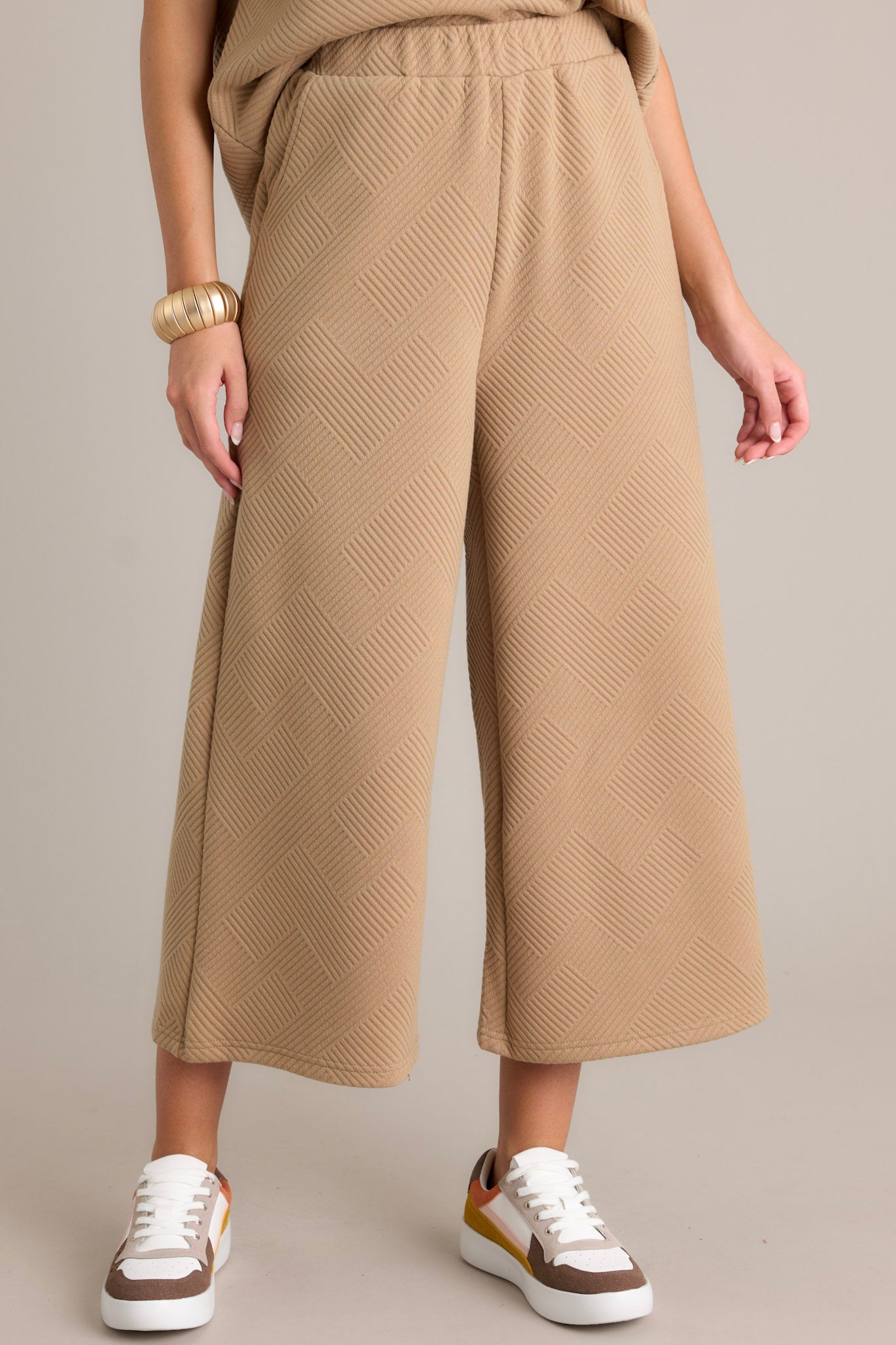 Detailed view of tan pants emphasizing the high-waisted design, textured crisscross pattern, elastic waistband, and wide-leg fit.