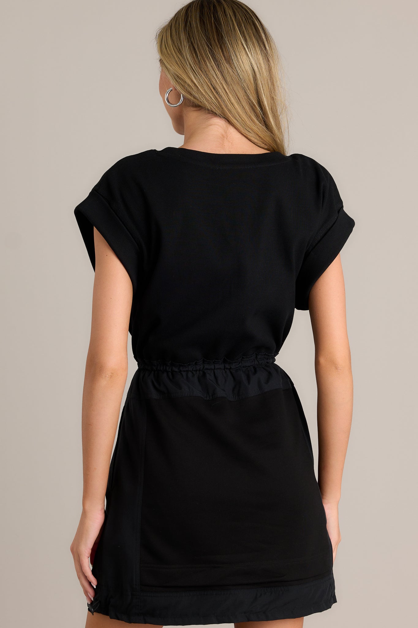 Back view of a black mini dress highlighting the overall fit, ribbed bodice, and adjustable hemline.