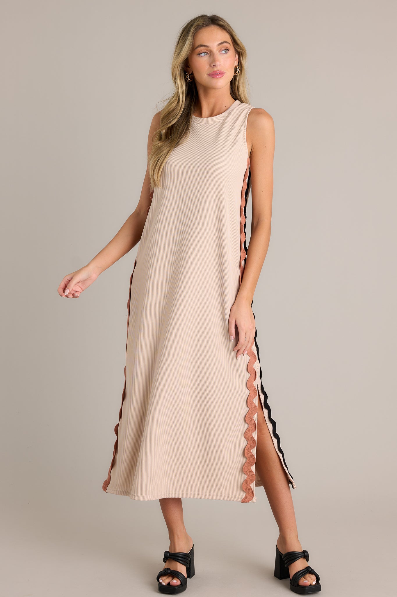 Front angled view of a taupe midi dress featuring a crew neckline, a ribbed material, two-toned ricrac side detailing, side slits, and a sleeveless design