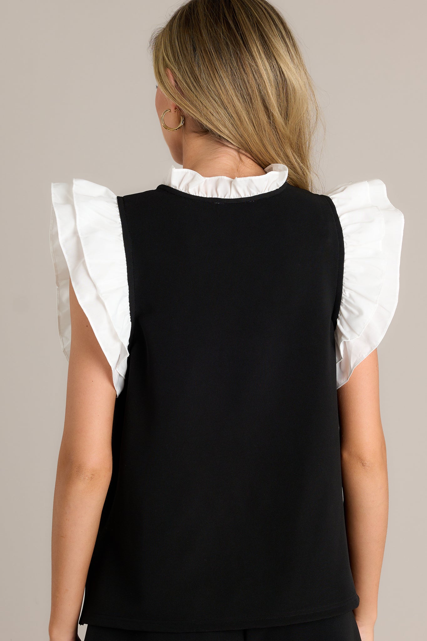 Back view of the top highlighting the continuation of the ribbed design and the side slits in the hem, with the ruffled collar adding a stylish detail