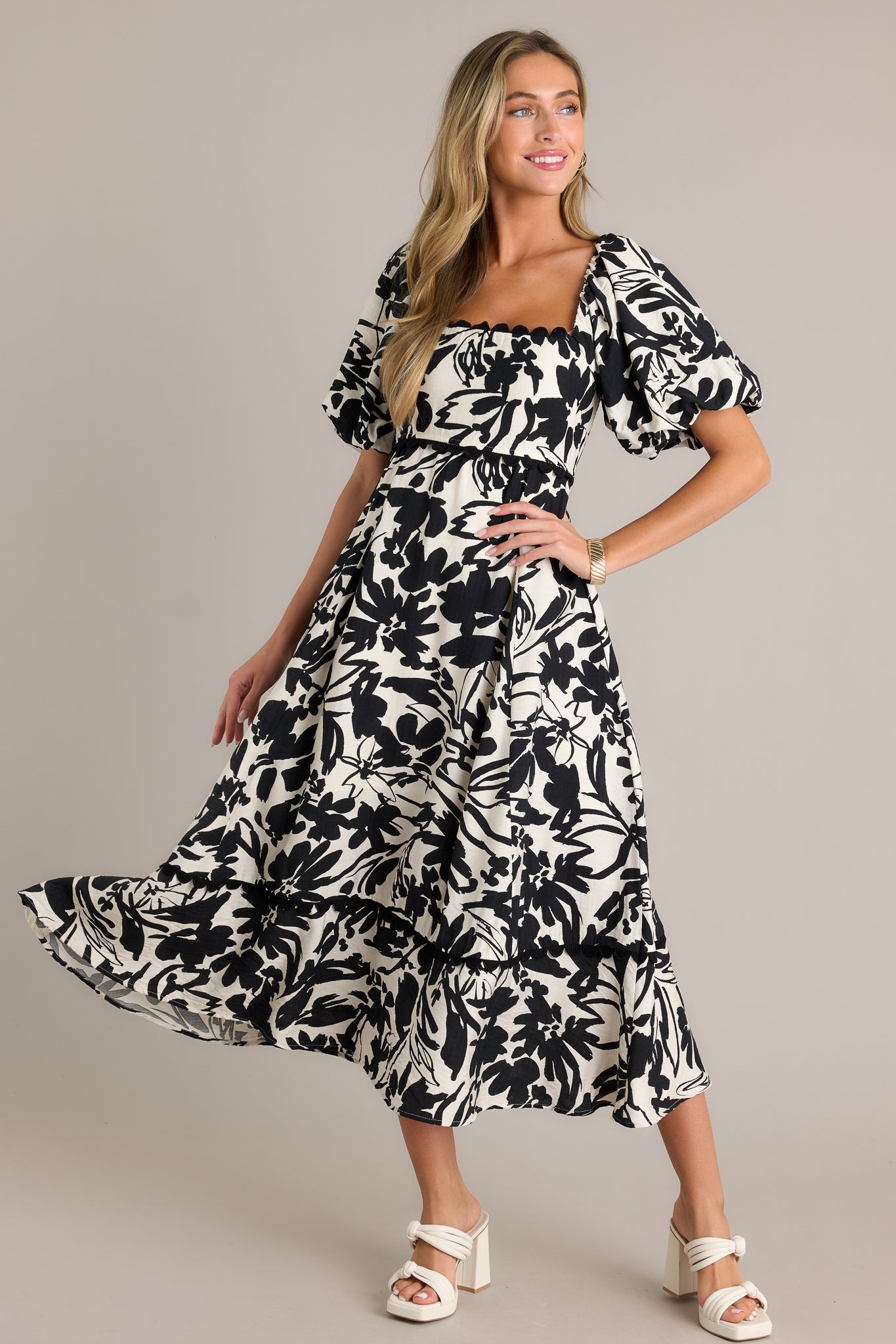 Action shot of an ivory maxi dress displaying the movement, highlighting the ruffled square neckline, functional hip pockets, smocked back insert, elastic cuffed puff sleeves, tiered design, and flowing silhouette.