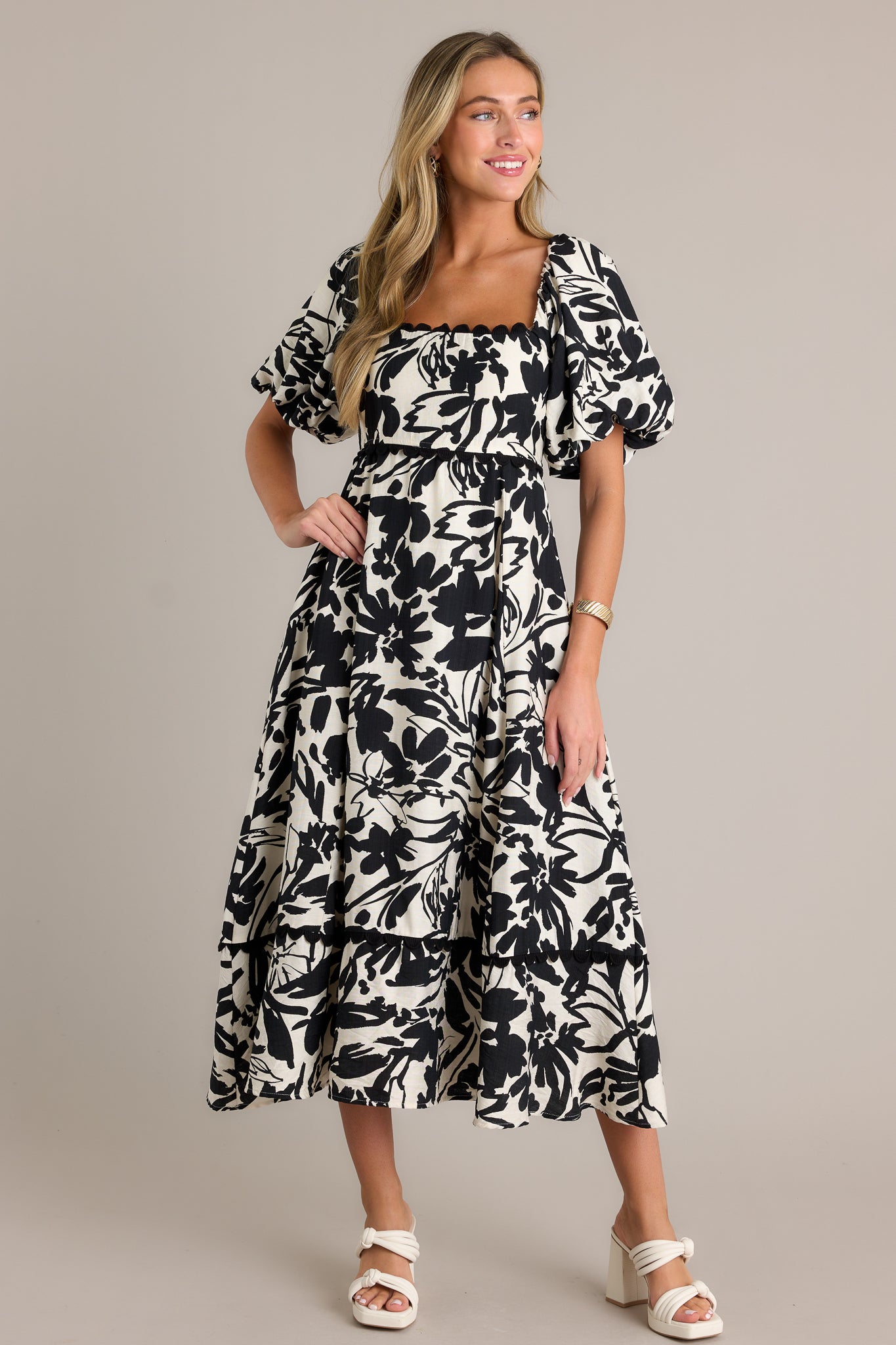 This ivory maxi dress features a ruffled square neckline, functional hip pockets, a smocked back insert, elastic cuffed puff sleeves, a tiered design, and a flowing silhouette.