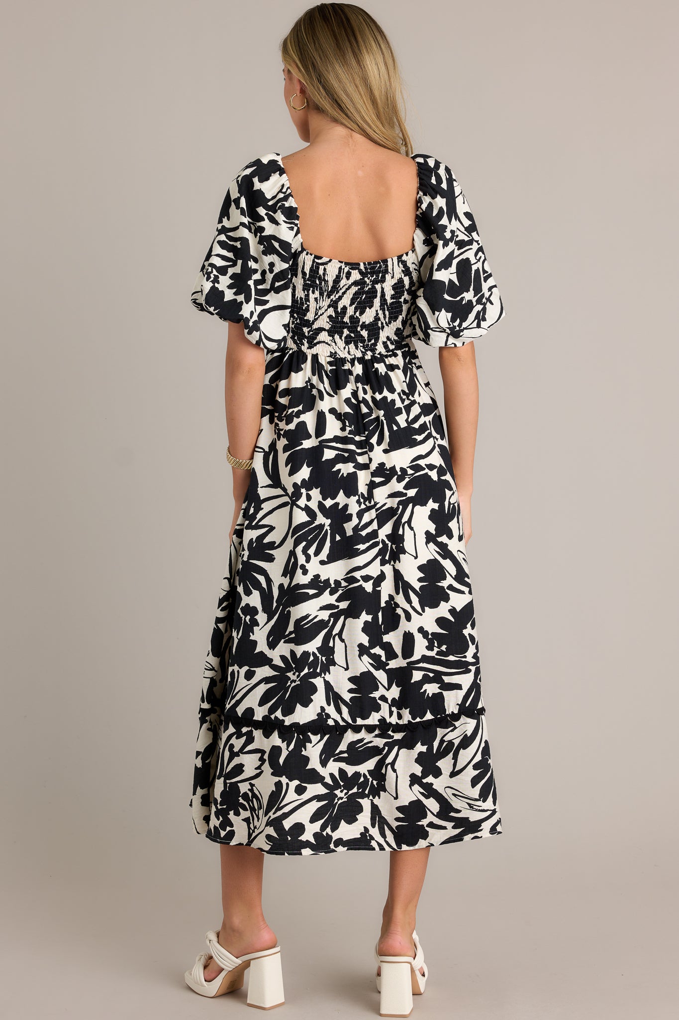 Back view of an ivory maxi dress emphasizing the smocked back insert, elastic cuffed puff sleeves, tiered design, and overall fit.