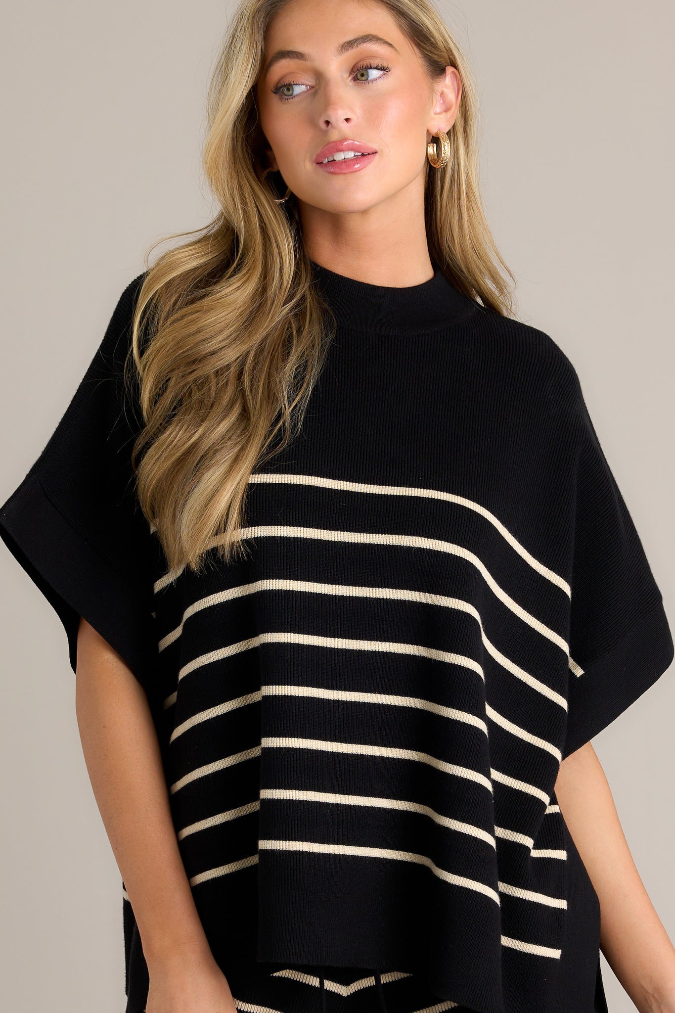 Front angled view of a stripe poncho top featuring a high neckline, high side slits, a classic stripe design, a thick hem, short sleeves, and an oversized fit