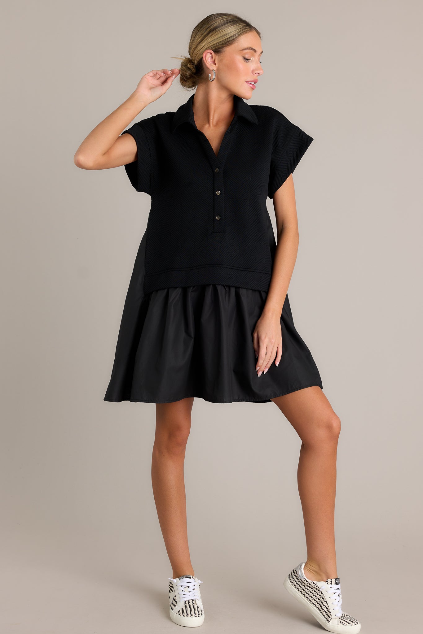 Action shot of a black quilted dress displaying the fit and movement, highlighting the collared v-neckline, functional button front, quilted bodice, tiered design, and short sleeves.