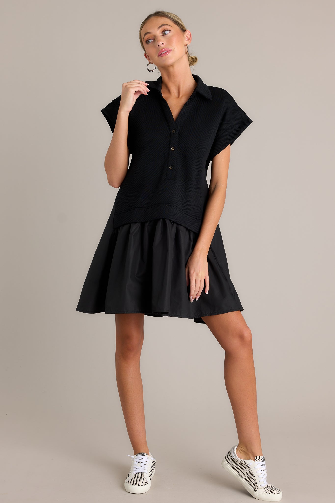 Front angled view of a black quilted dress featuring a collared v-neckline, a functional button front, a quilted bodice, a tiered design, and short sleeves