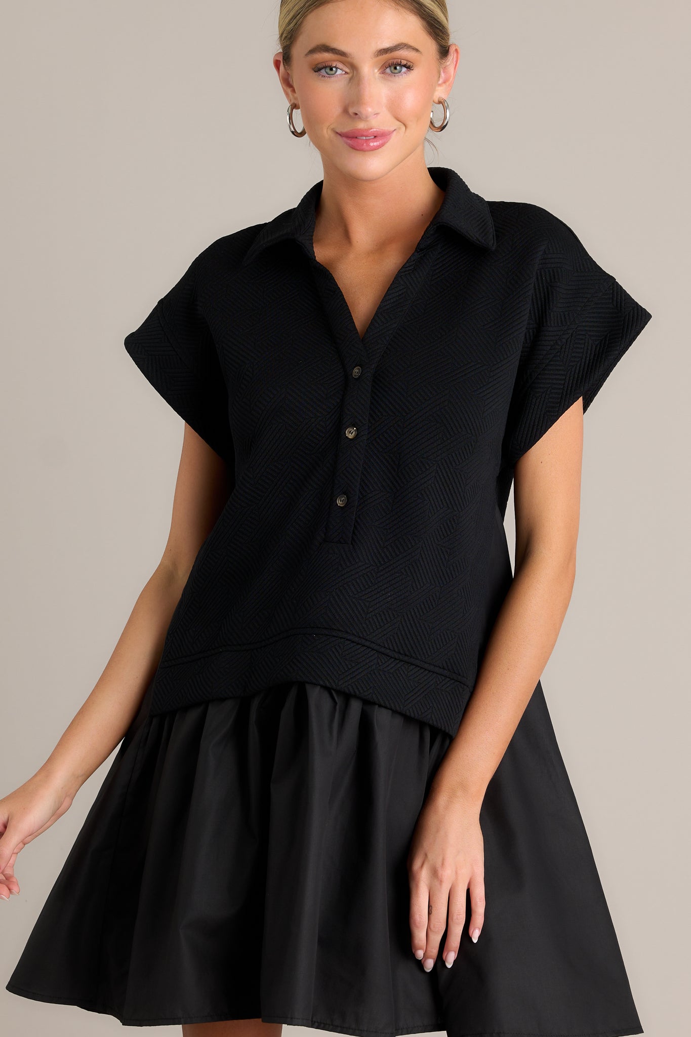 This black quilted dress features a collared v-neckline, a functional button front, a quilted bodice, a tiered design and short sleeves.