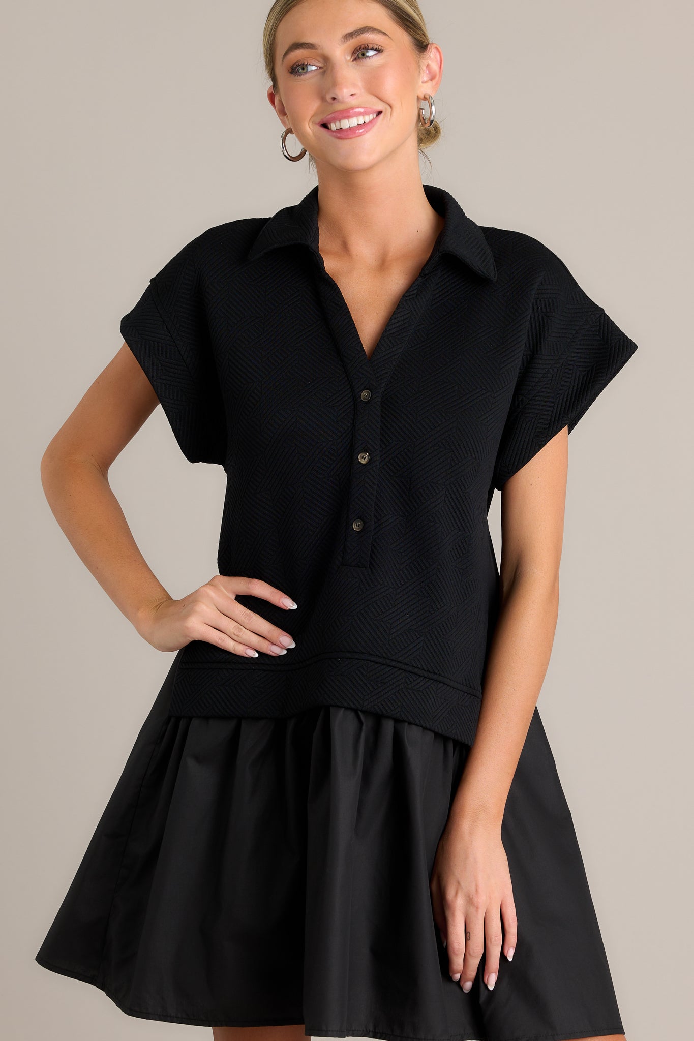 Front view of a black quilted dress featuring a collared v-neckline, a functional button front, a quilted bodice, a tiered design, and short sleeves.