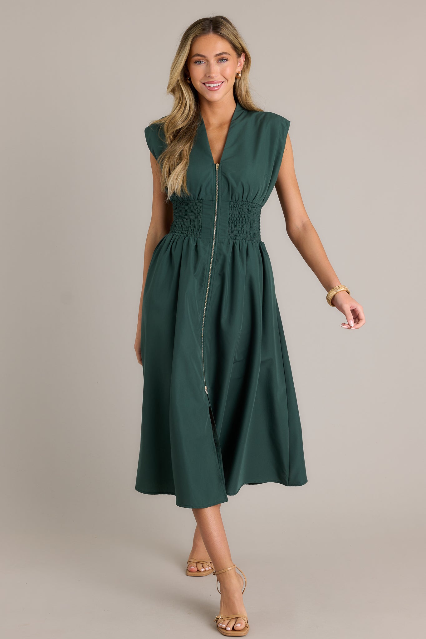 Action shot of a hunter green midi dress displaying the fit and movement, highlighting the v-neckline, padded shoulders, full zipper front, fully smocked waist, functional hip pockets, and front slit.