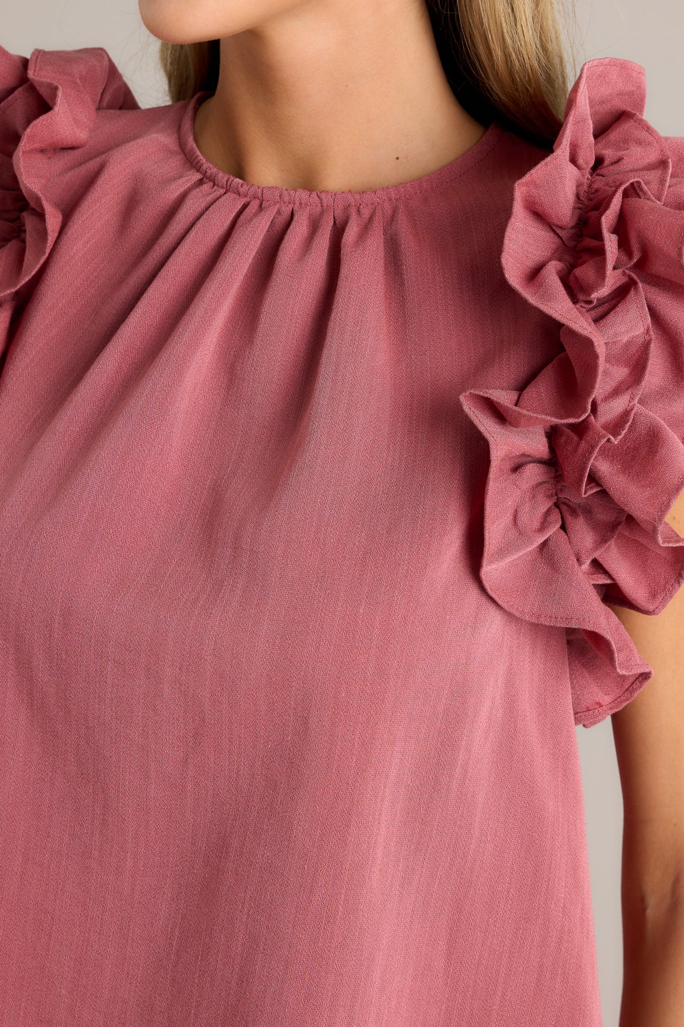 Close-up of the rose top showing the high crew neckline and ruffled shoulder detailing.