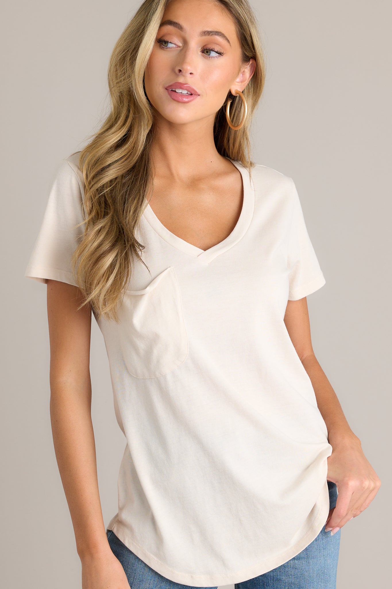 Front angled view of a tee featuring a v-neckline, a slouched breast pocket, a scooped hemline, and short sleeves